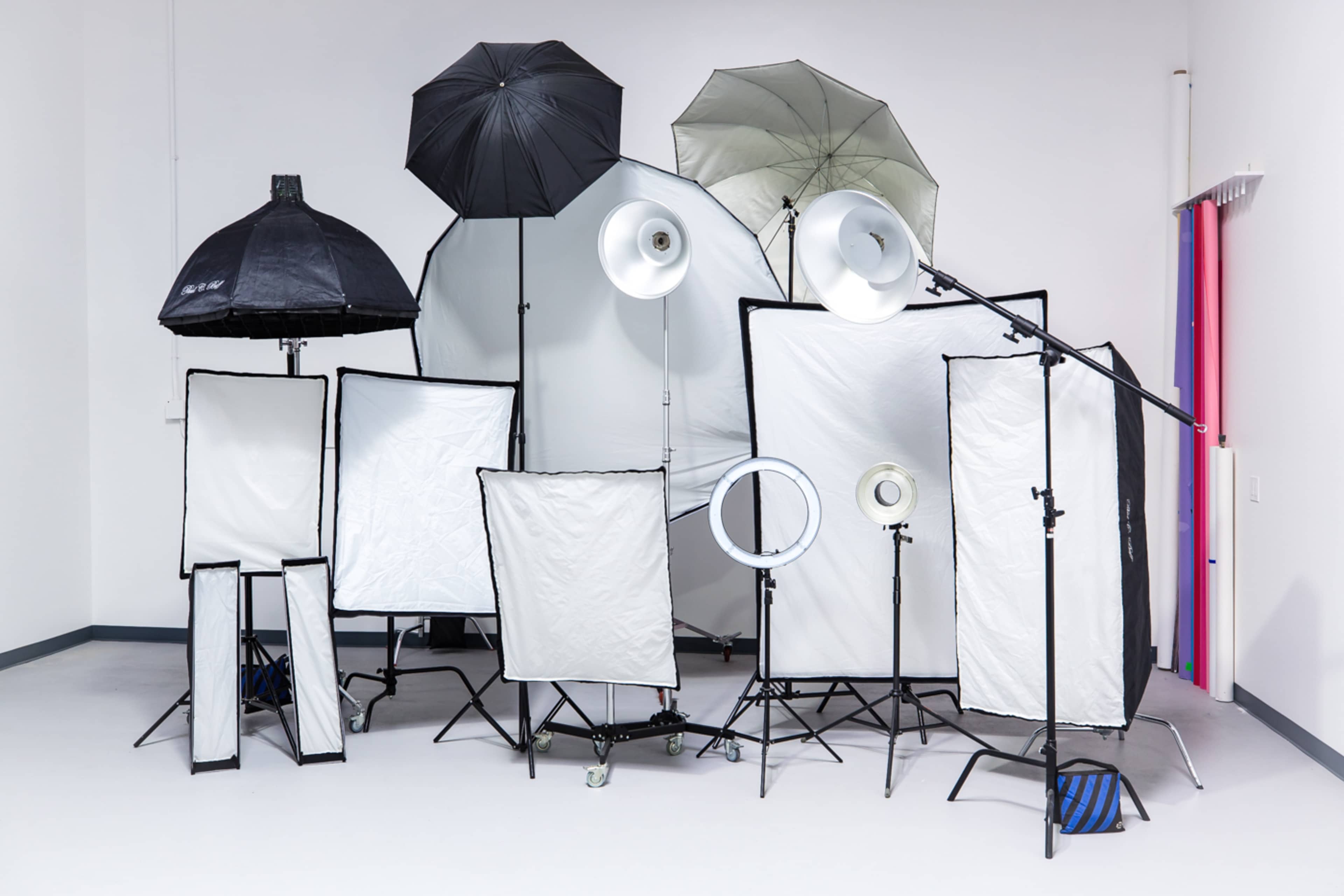 A collection of various photography lighting equipment and modifiers is arranged in a studio setting.