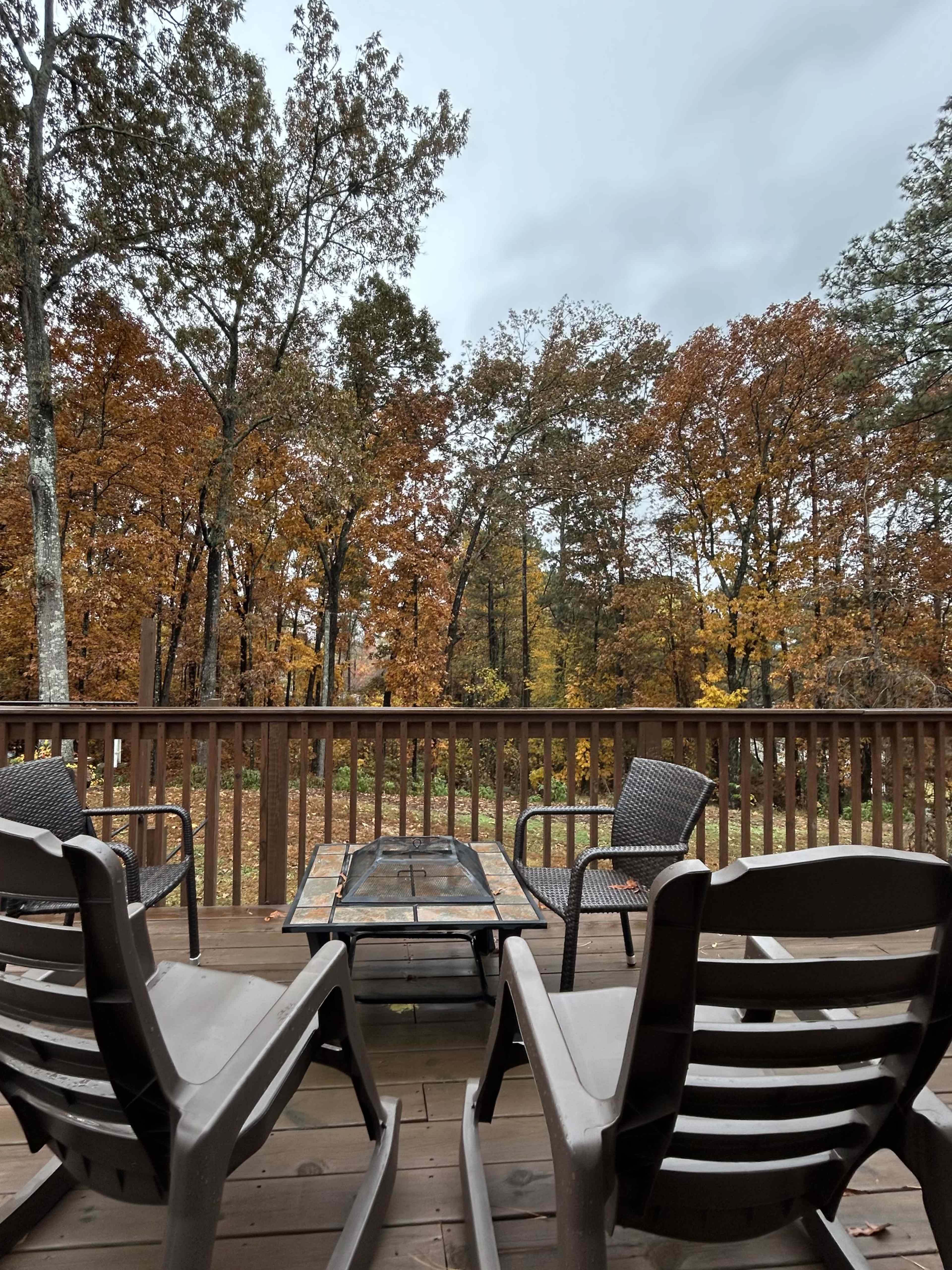 A deck with two chairs and a glass-topped table overlooks a forest of trees with autumn foliage.