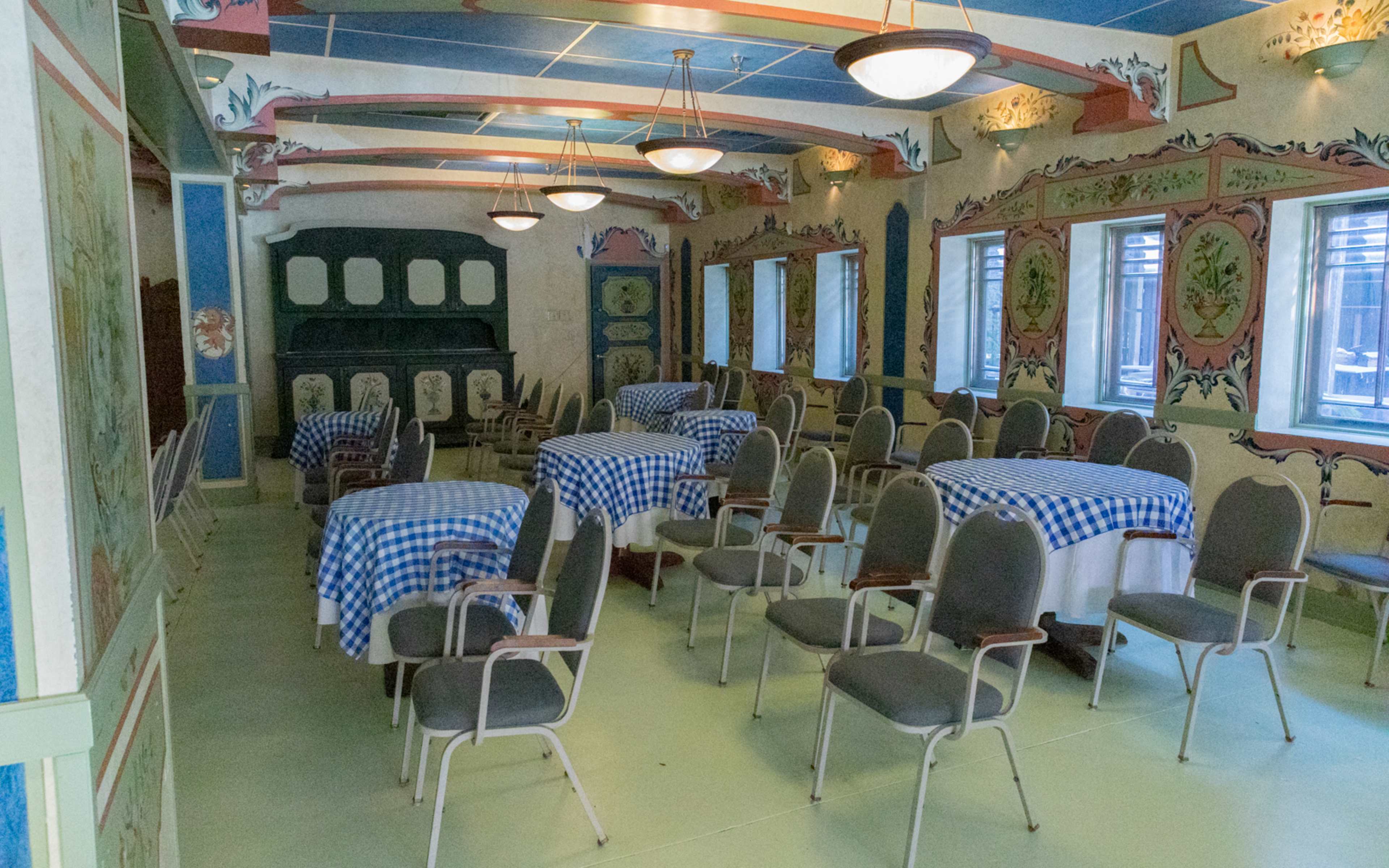 A dining room with checkered tablecloths on several tables, surrounded by green and blue decor and rows of chairs.