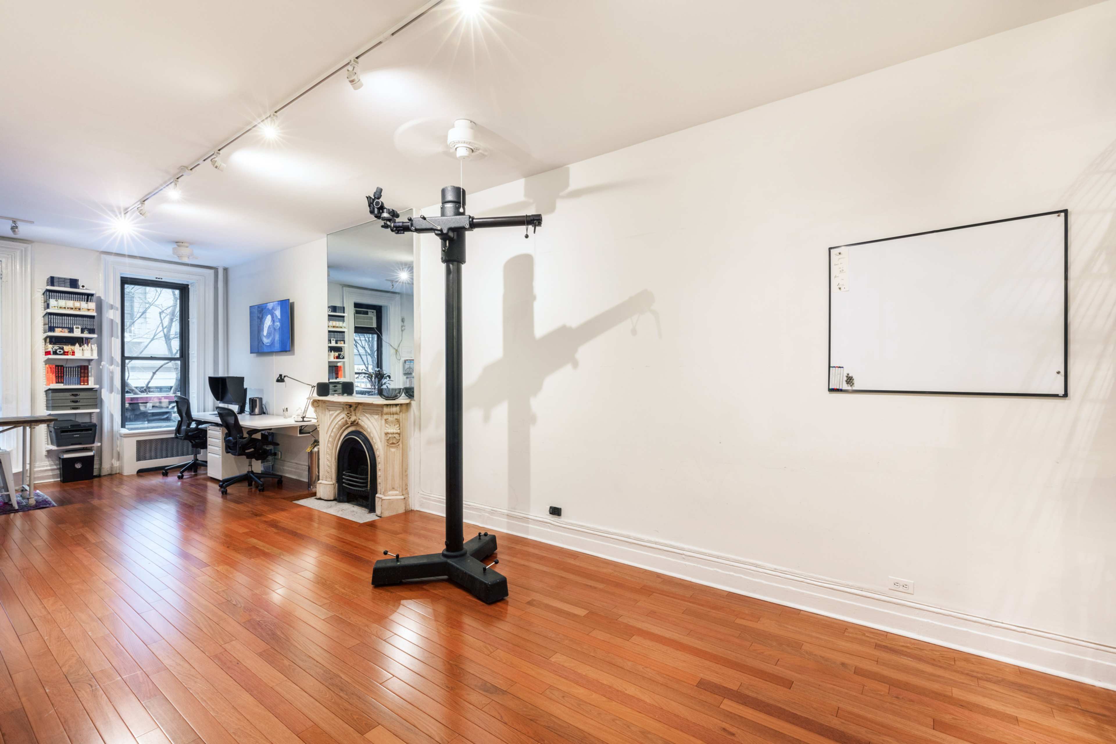 A spacious room with hardwood floors featuring a white wall, a freestanding equipment stand, a whiteboard, and a fireplace.
