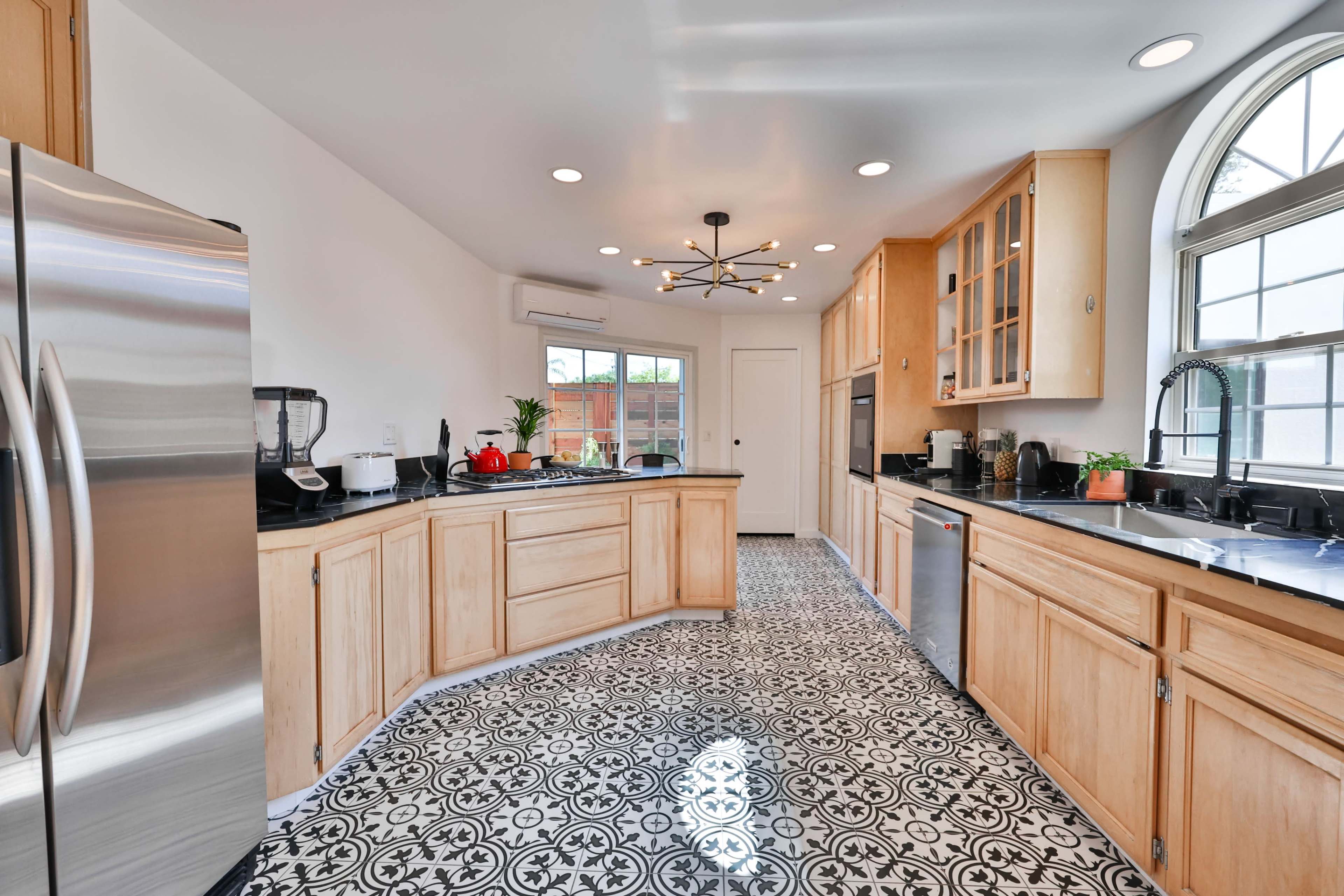 A modern kitchen with wooden cabinets, stainless steel appliances, and patterned black-and-white tile flooring.