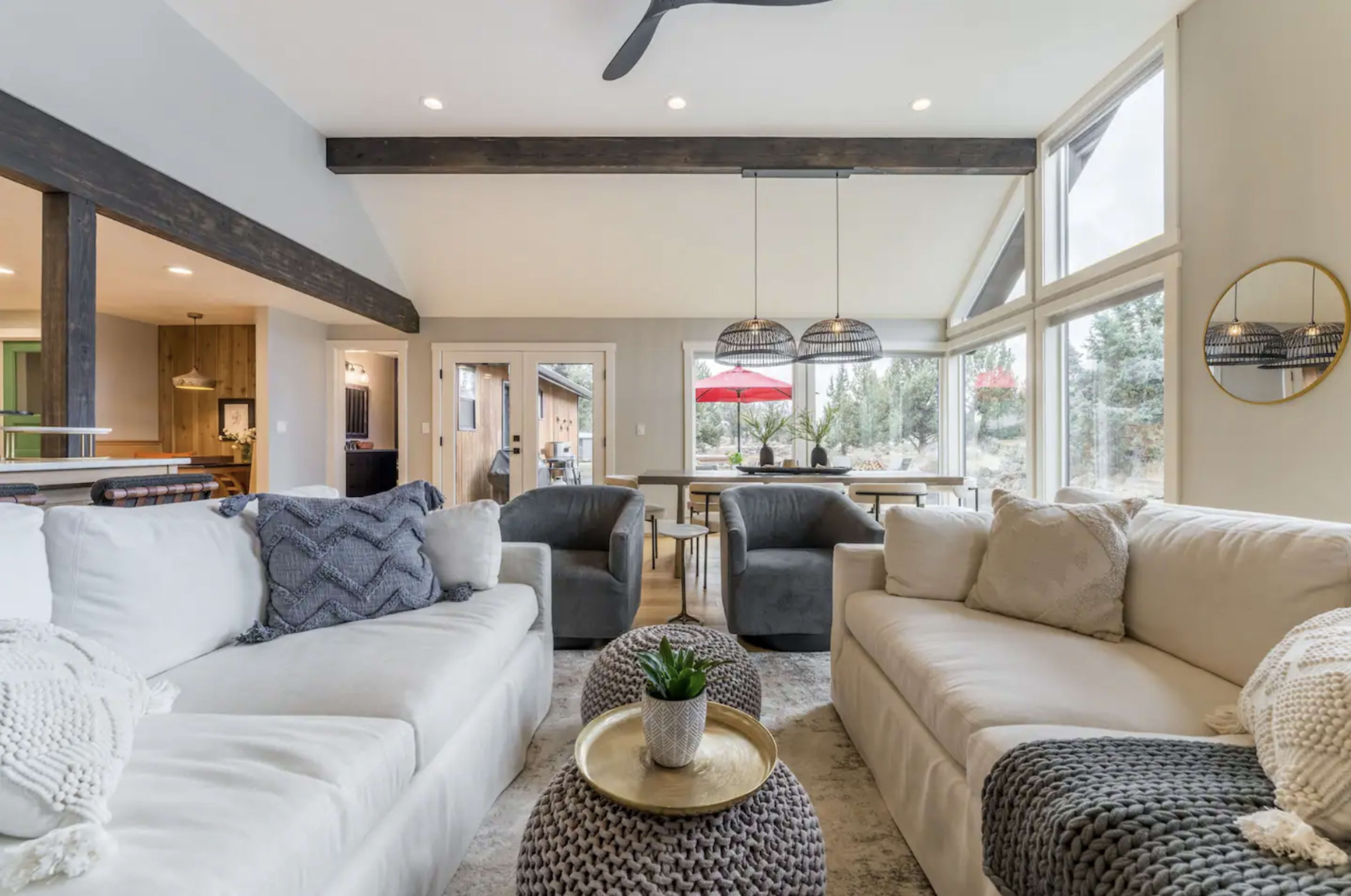 A modern living room with two light-colored sofas, a coffee table, and large windows overlooking a patio area with outdoor seating.