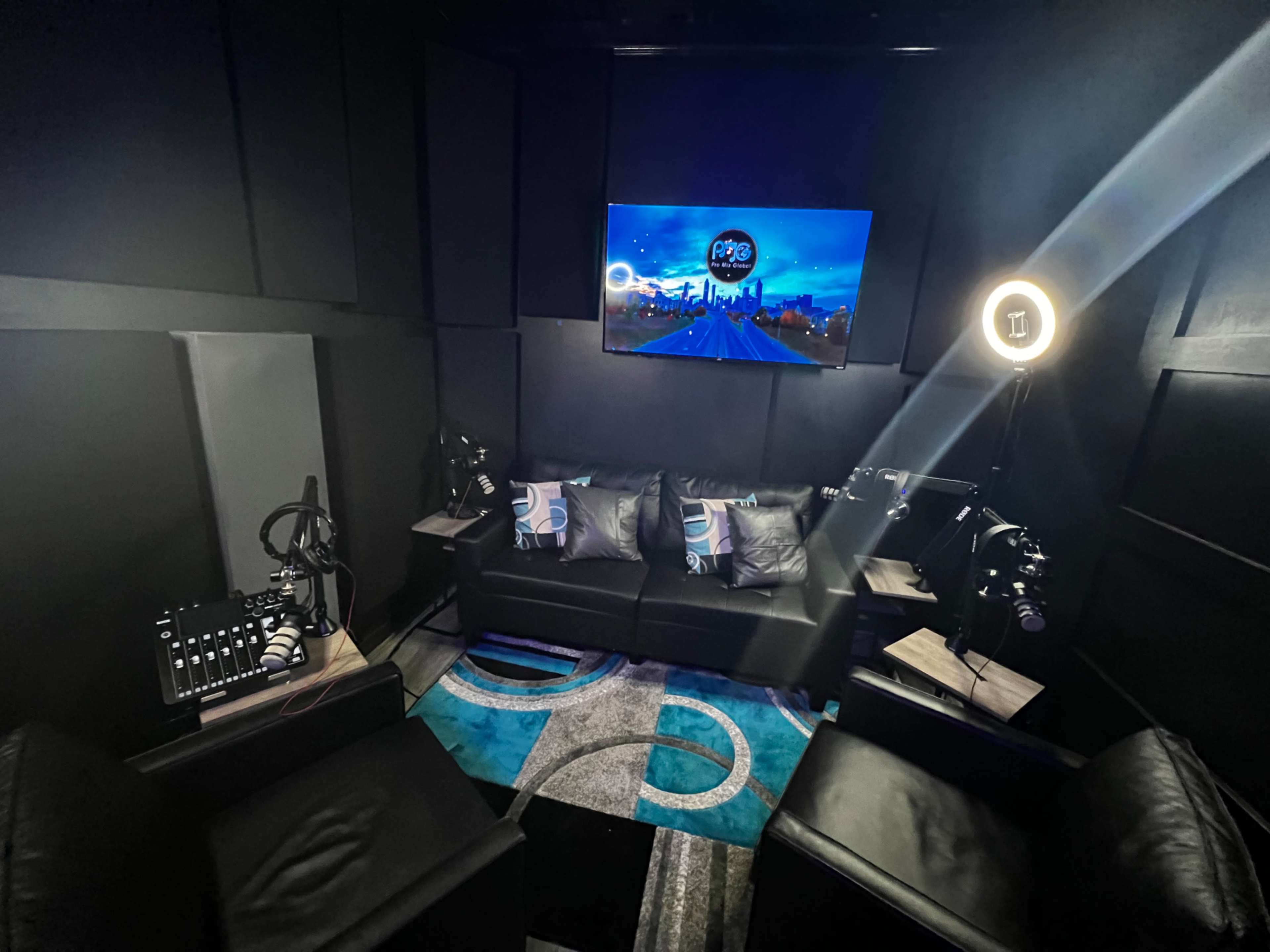 A recording studio with a sofa, two chairs, and technical equipment, all surrounded by soundproofing panels.