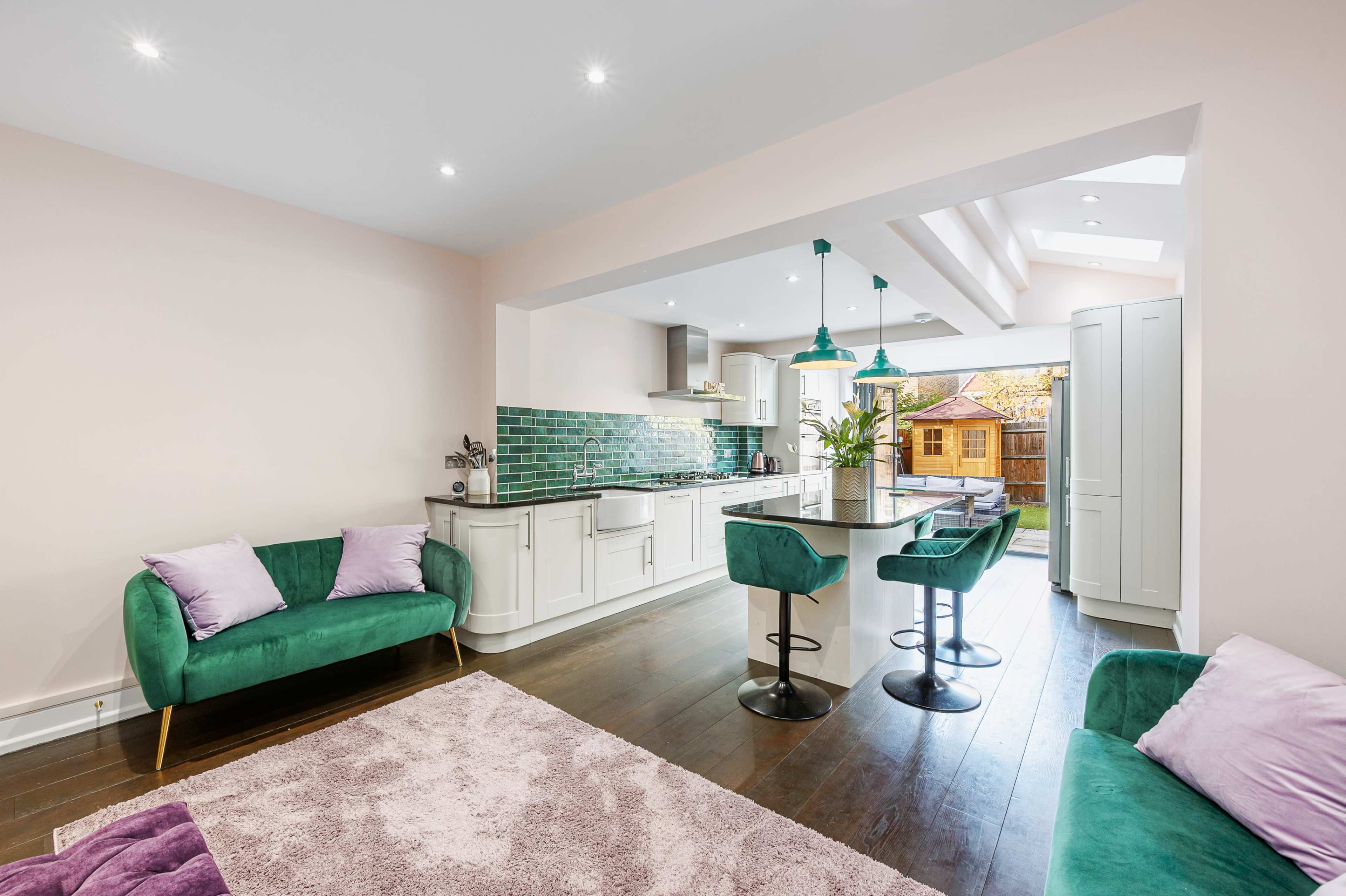 A modern kitchen features green accents, a bar with stools, and a spacious layout with large windows.