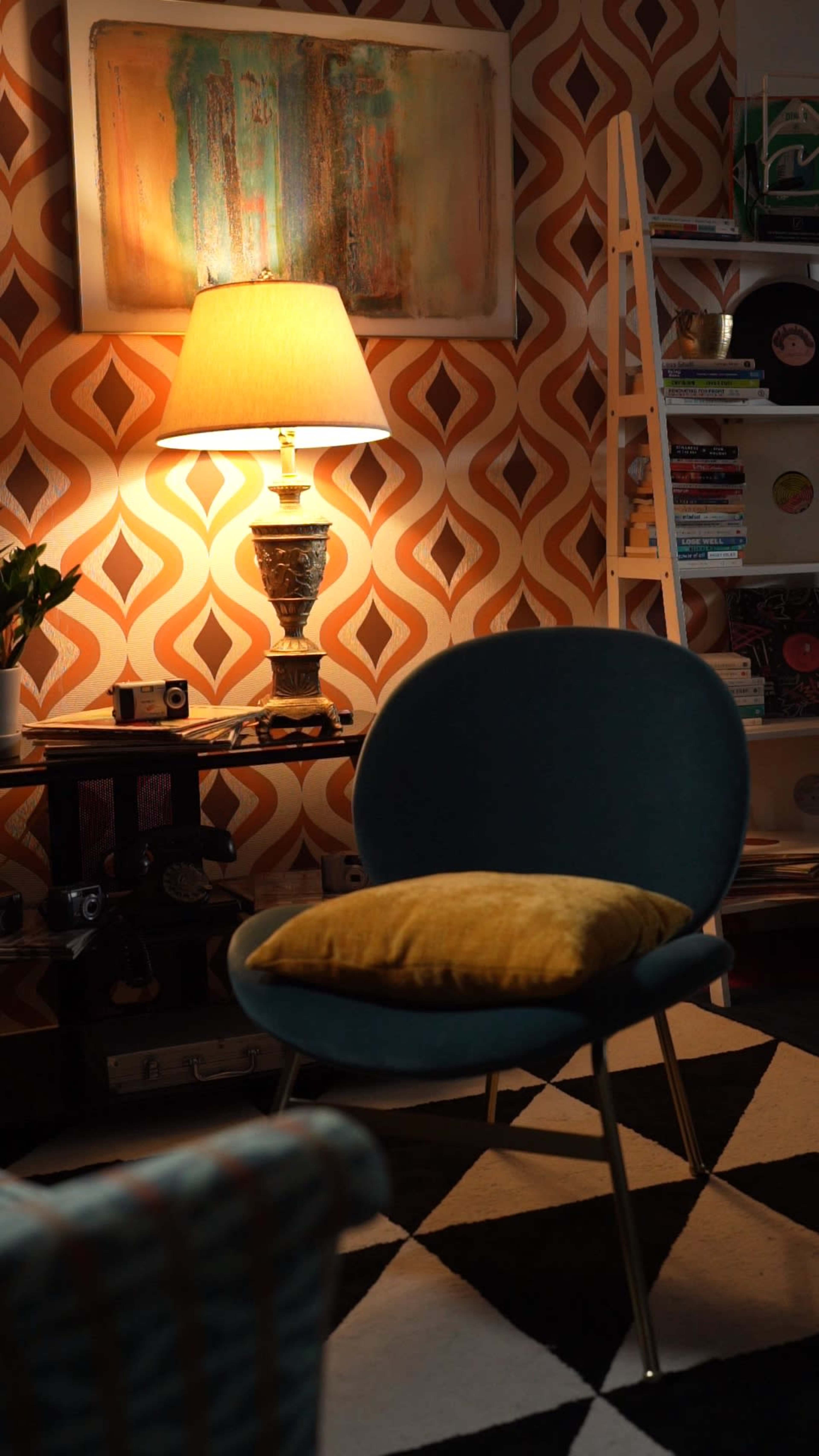 A stylish room features an illuminated lamp beside a blue chair with a yellow cushion, against a patterned wallpaper and contrasting black and white floor.