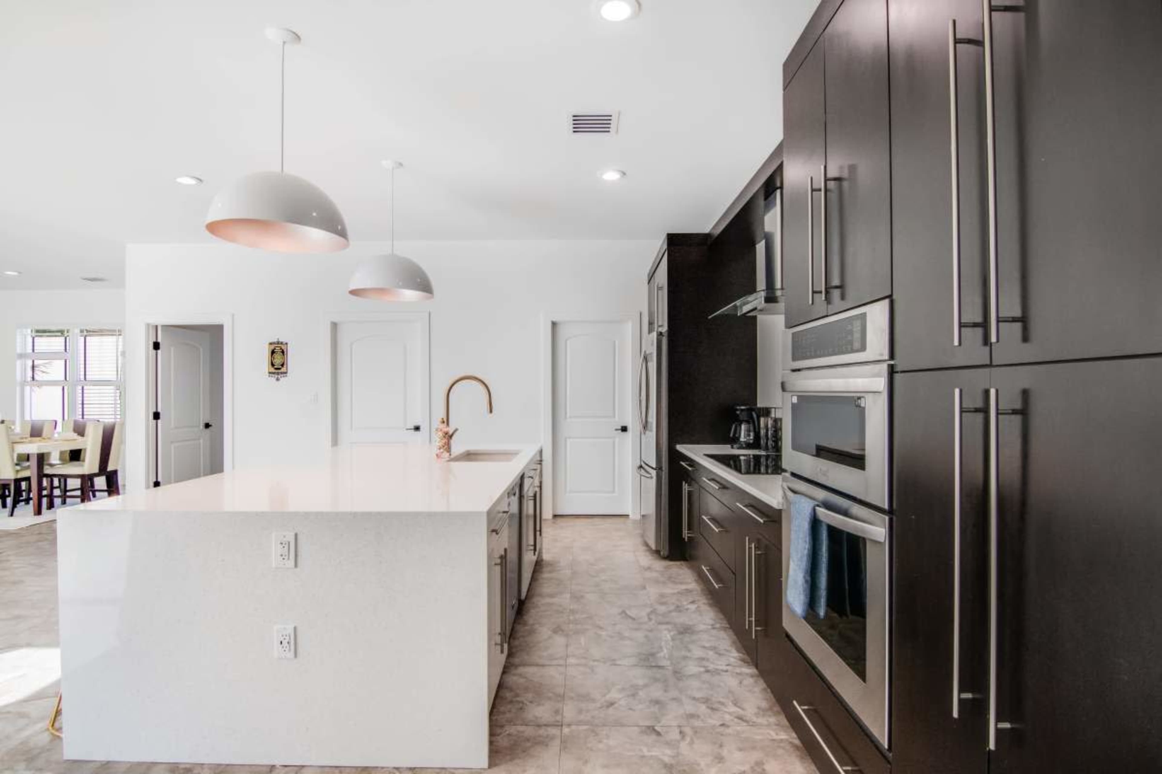 A modern kitchen featuring dark cabinetry, a large white island with pendant lighting, and stainless steel appliances.