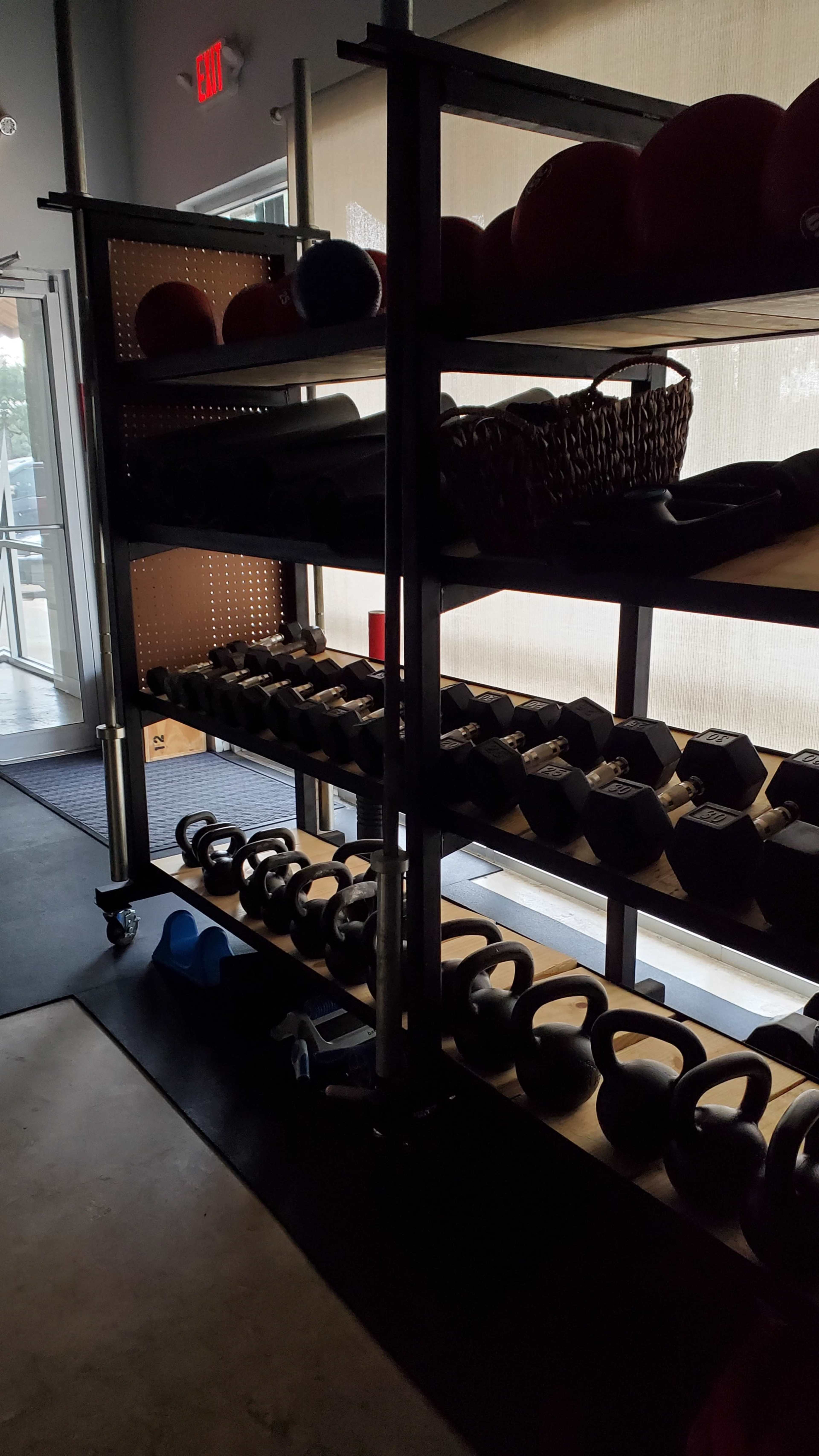 A shelf with various weights, including kettlebells and dumbbells, in a dimly lit fitness facility.