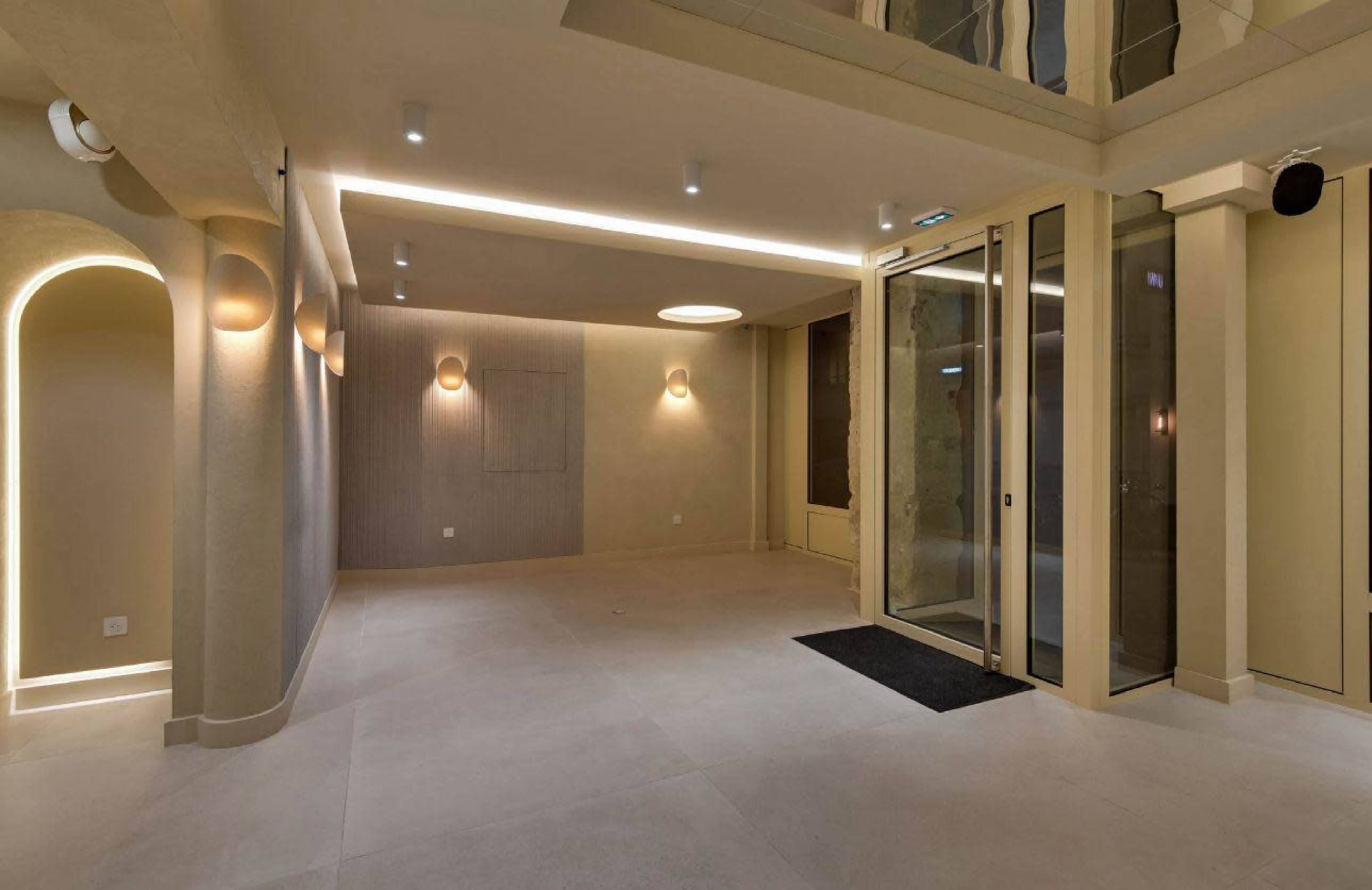 The image shows a spacious, modern interior with neutral-colored walls, recessed lighting, and a glass entrance.