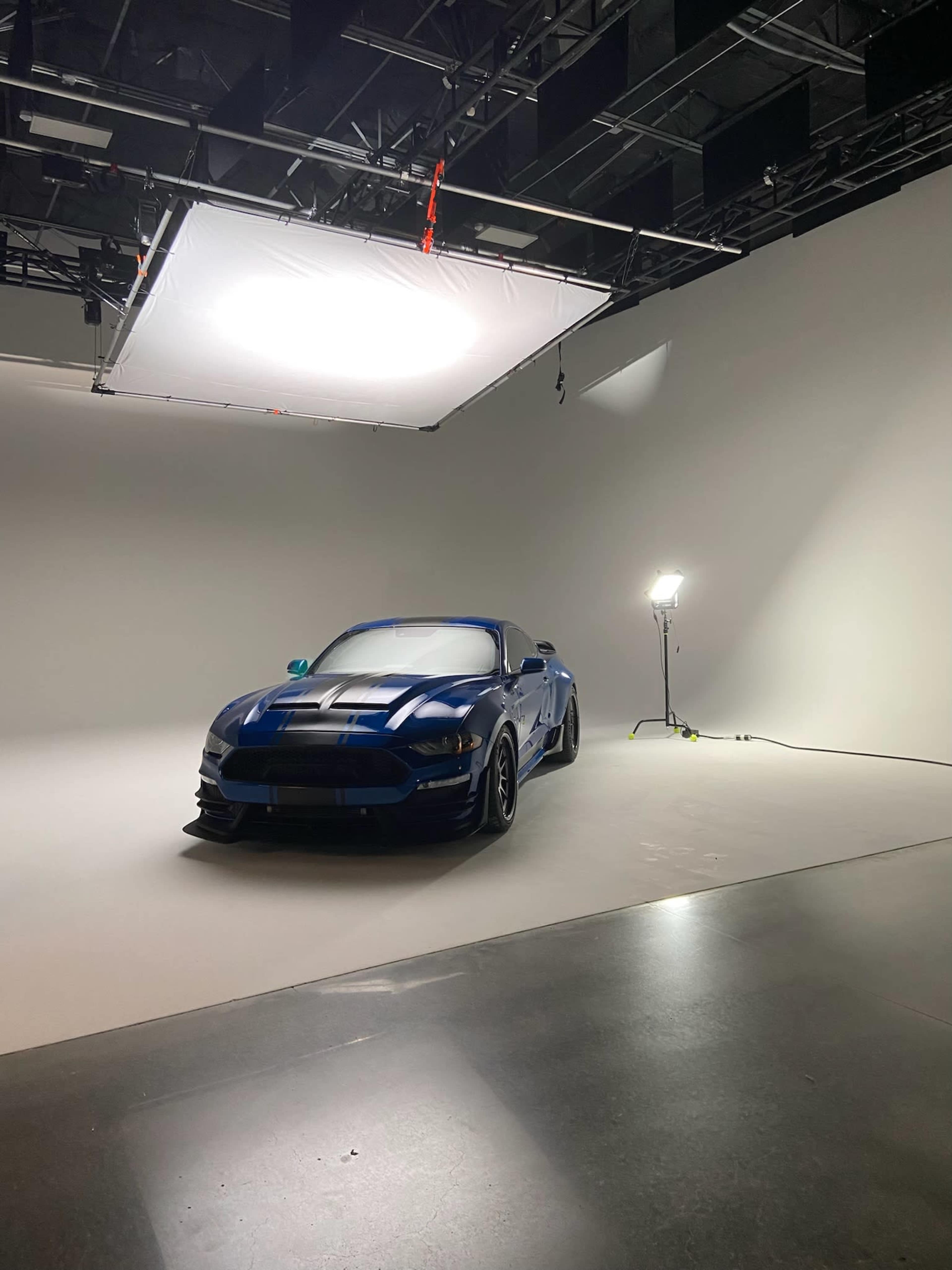 A blue sports car is positioned in a well-lit studio with a plain white backdrop.