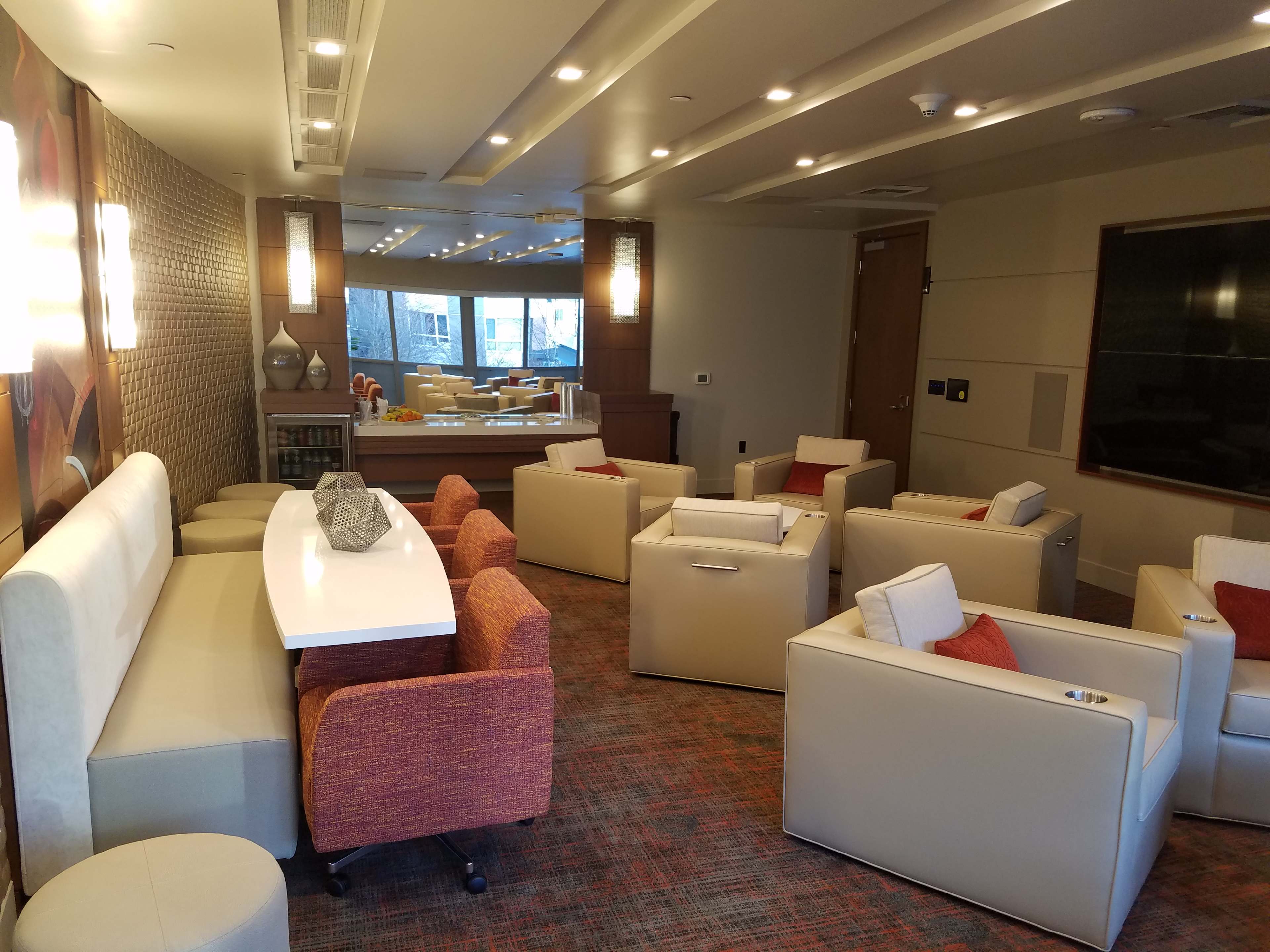 A lounge area features modern furniture, including armchairs and a communal table, with a large mirror reflecting the space.