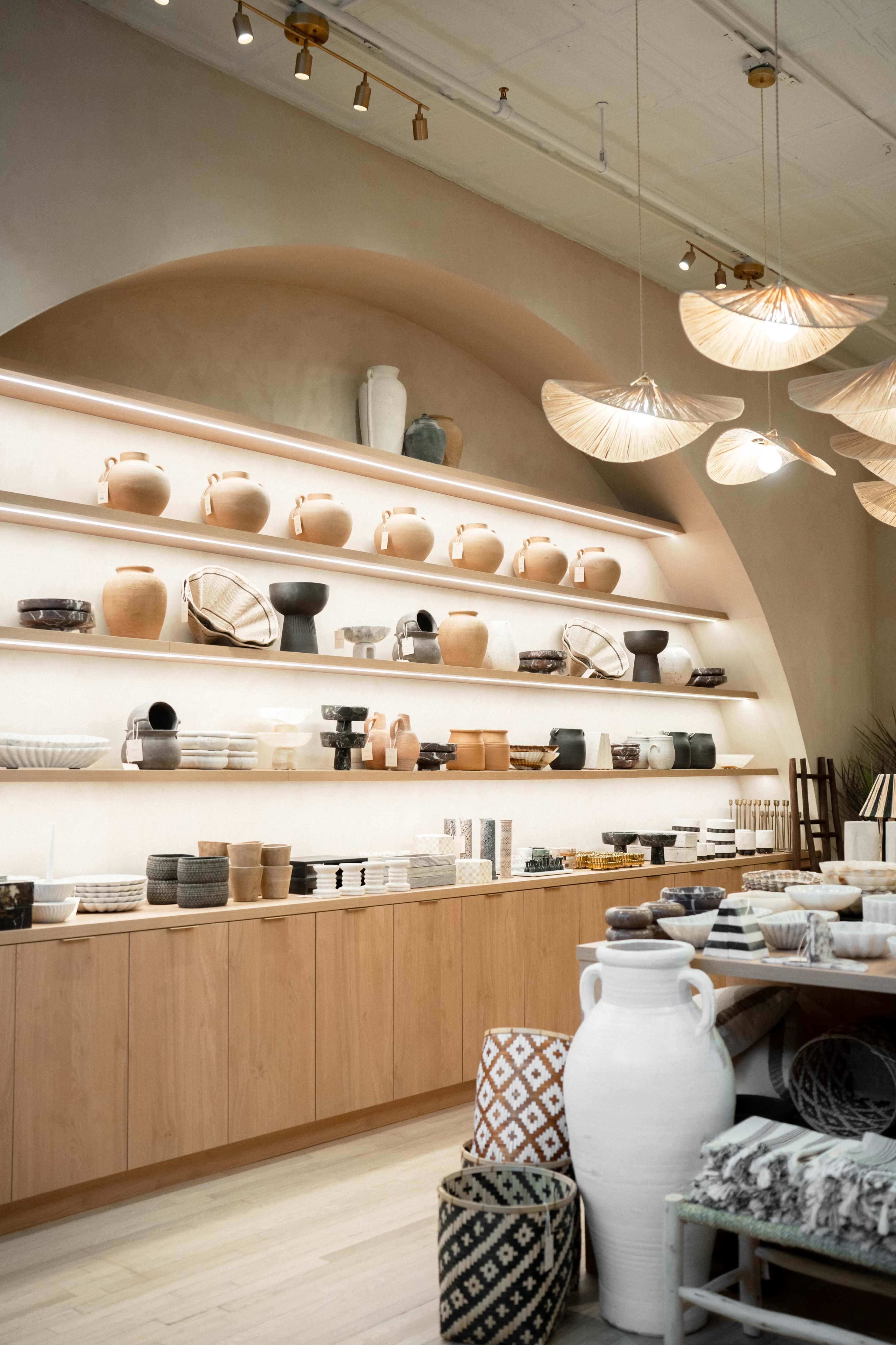A well-organized shop displays various pottery and home decor items on shelves and tables against a minimalist backdrop.