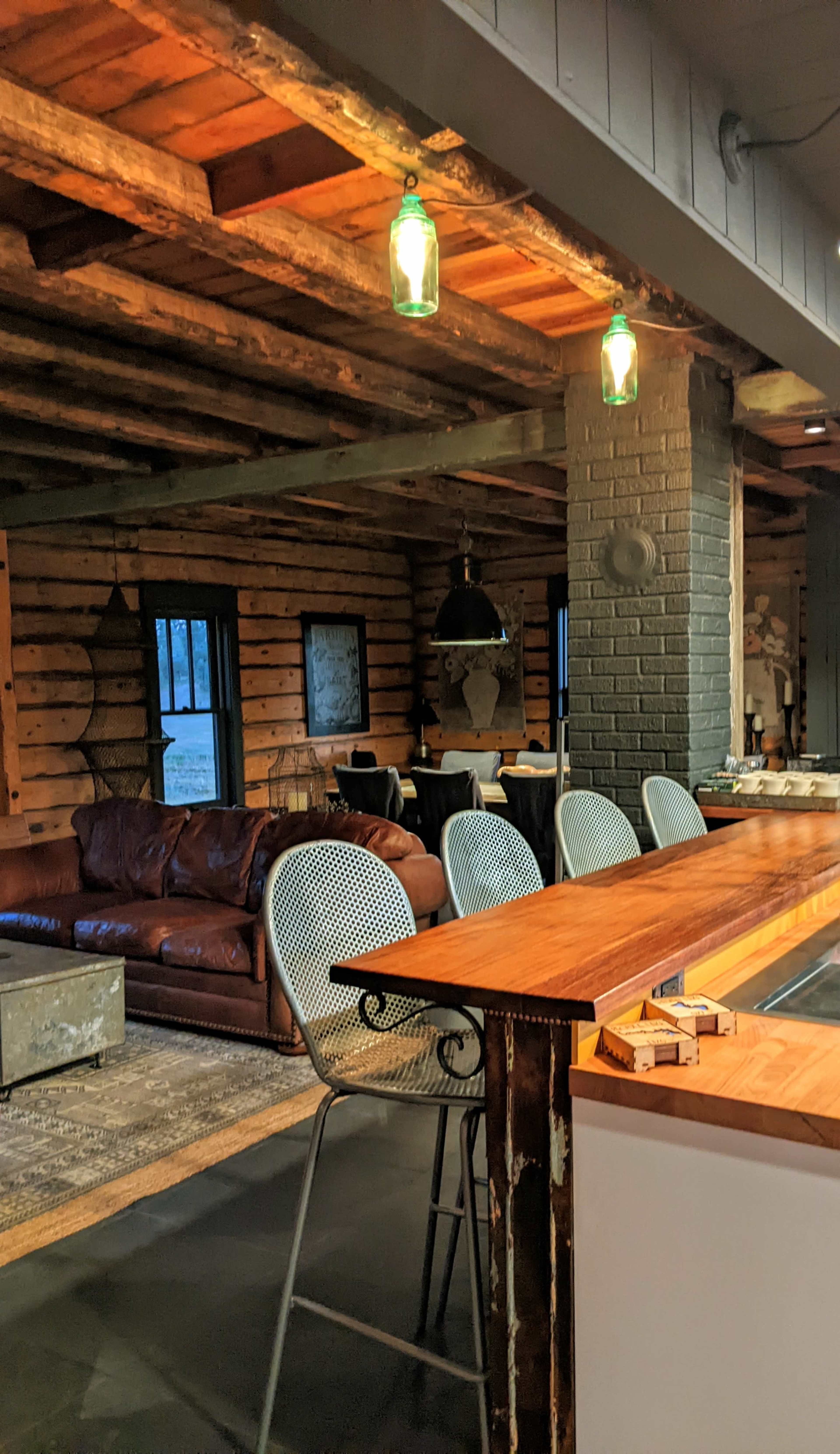 A rustic interior of a cabin with a wooden ceiling, a leather sofa, and a bar with metal stools.