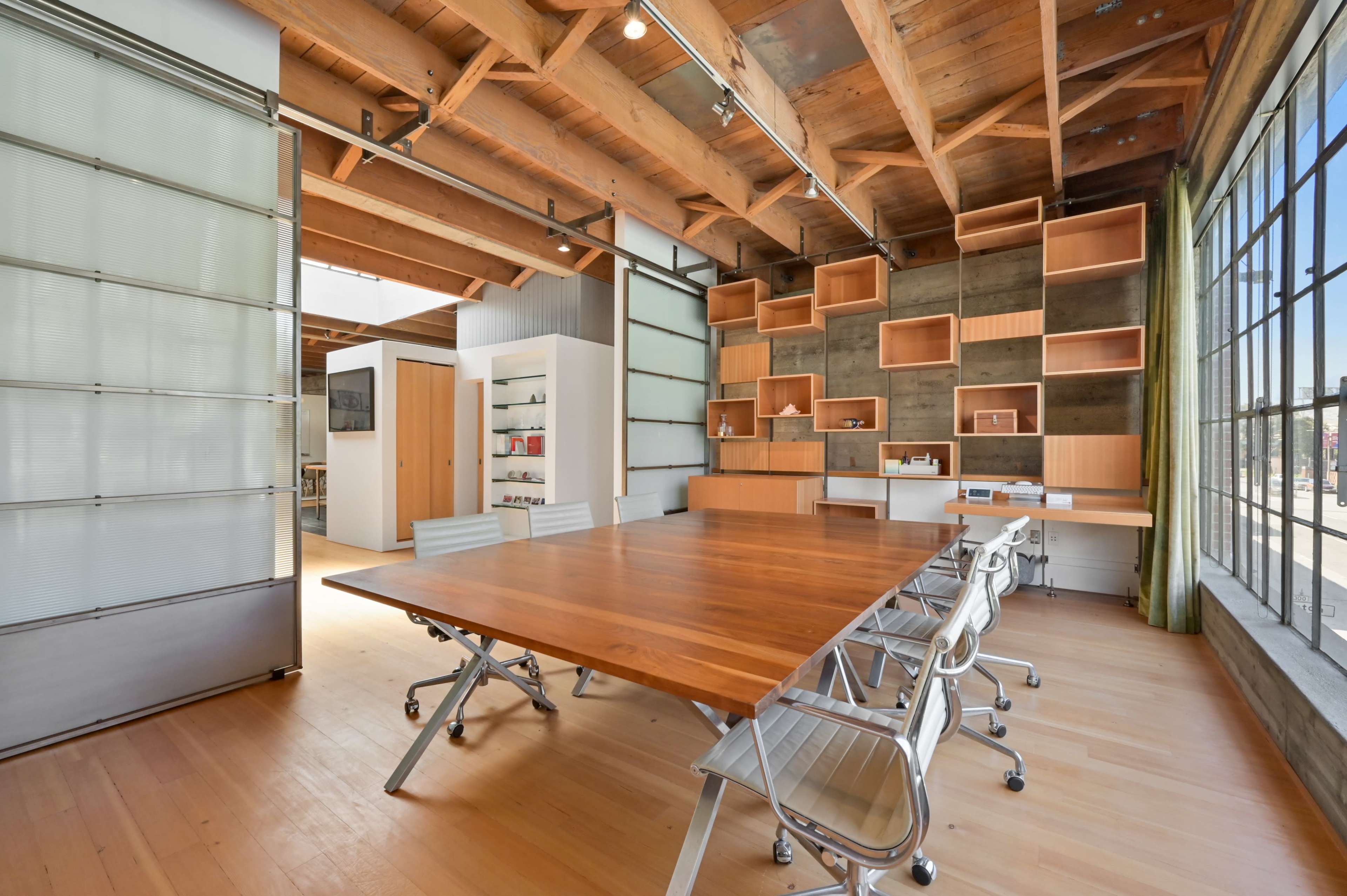 A modern office space with a large wooden table and sleek chairs, surrounded by wooden beams and shelving.