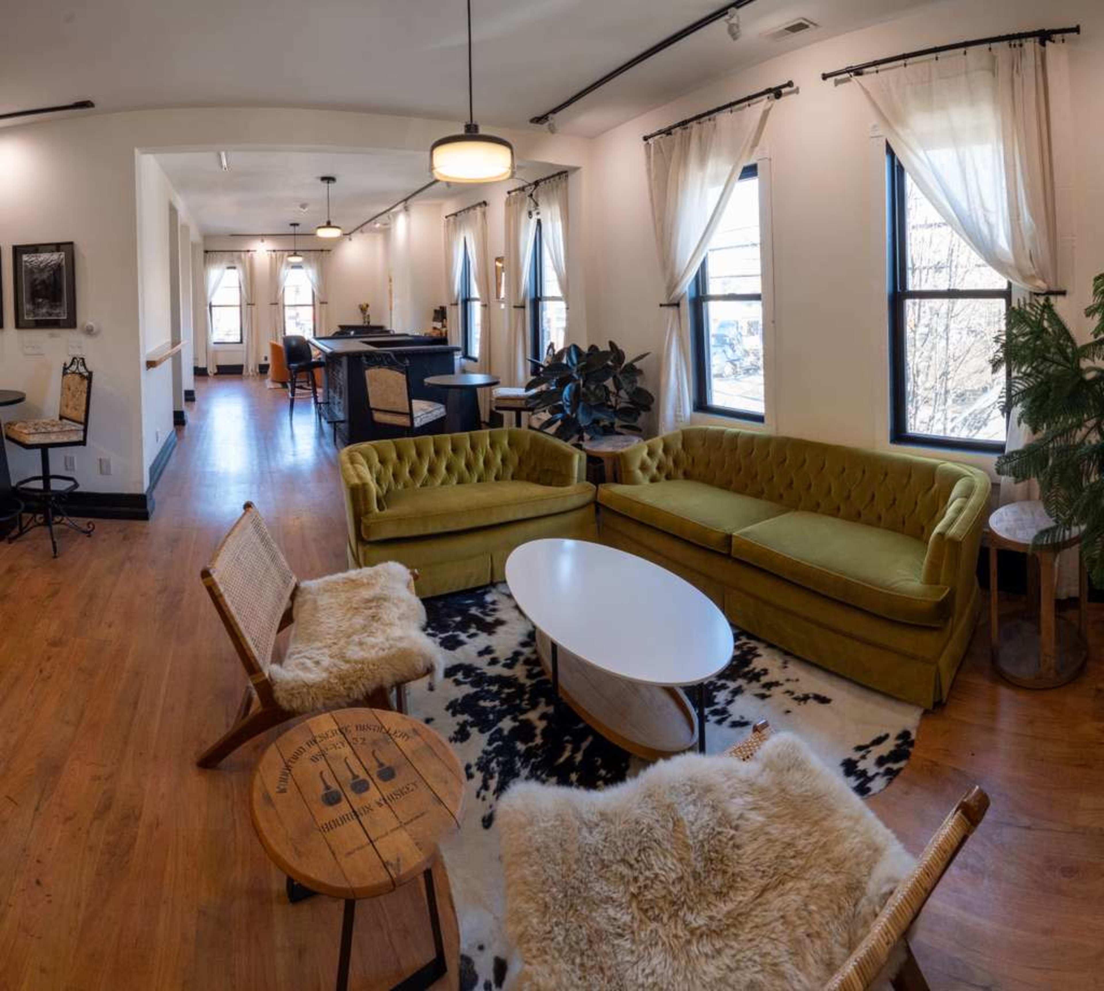 A cozy lounge area features a green velvet sofa, wooden chairs with soft coverings, and a round coffee table on a cowhide rug.