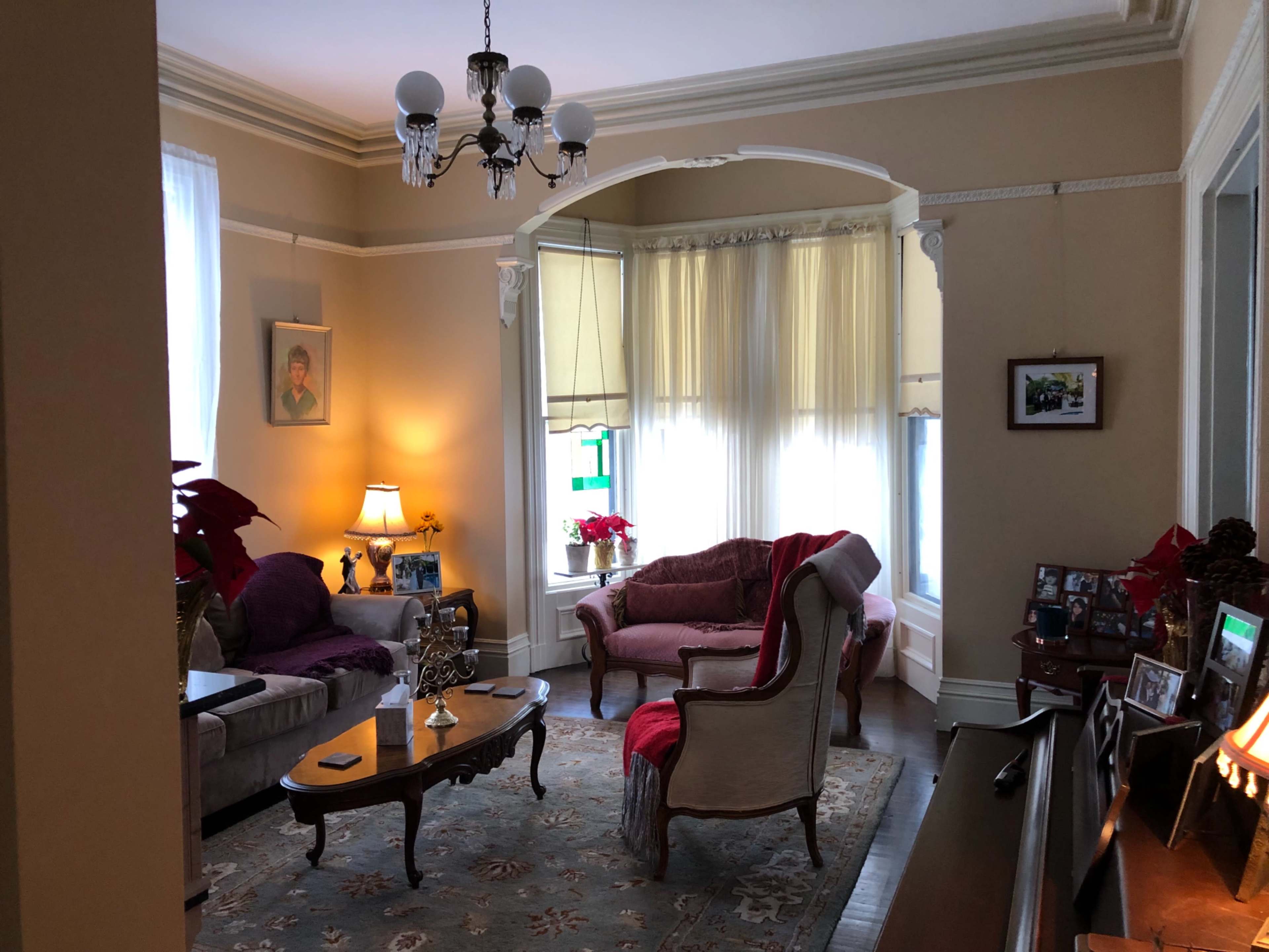 A cozy living room with a chandelier, a sofa, and a chair arranged around a coffee table, complemented by large windows and various decorations.