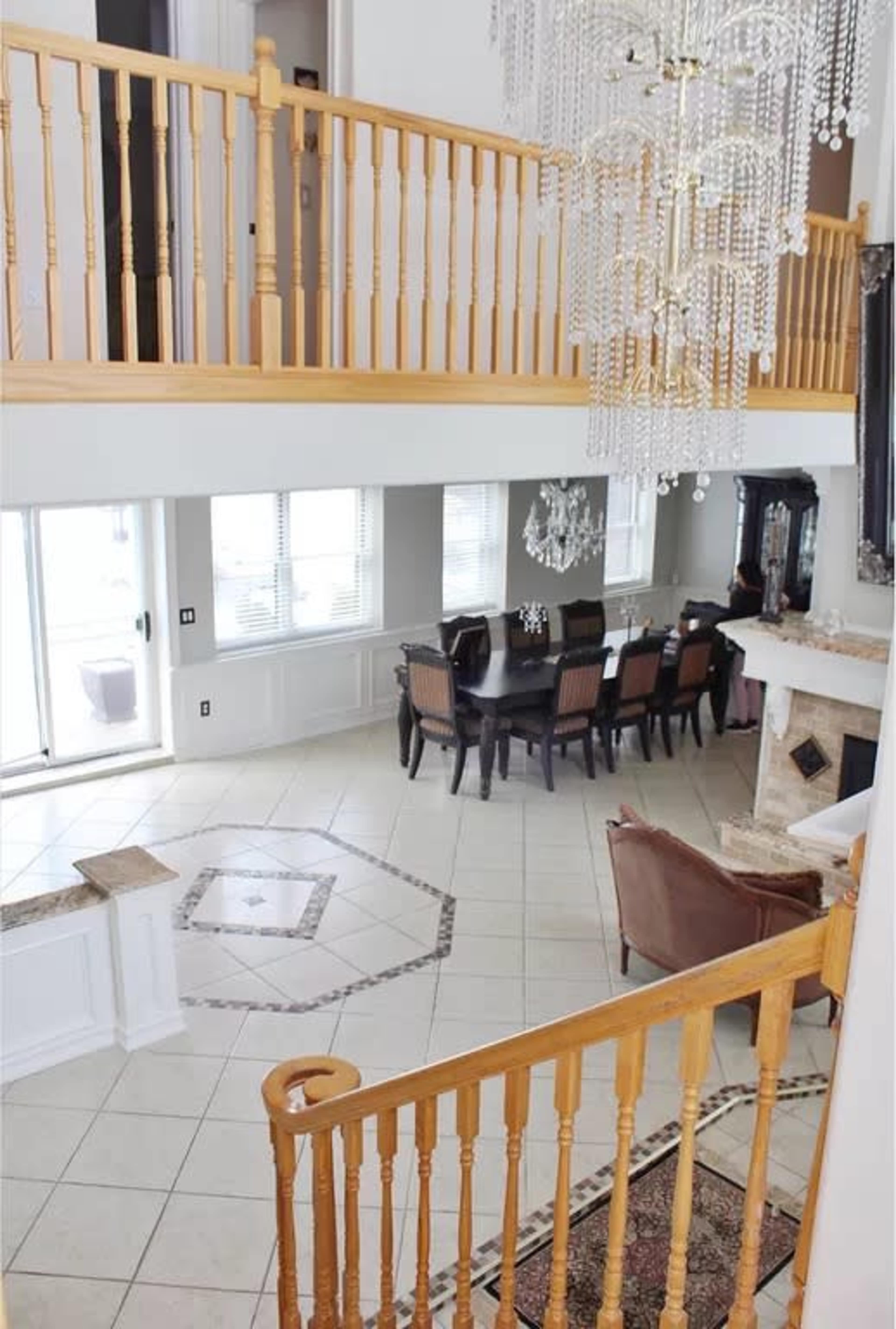 The image shows a spacious, two-story entrance hall with a staircase and a view of a dining area featuring a large table and a chandelier.