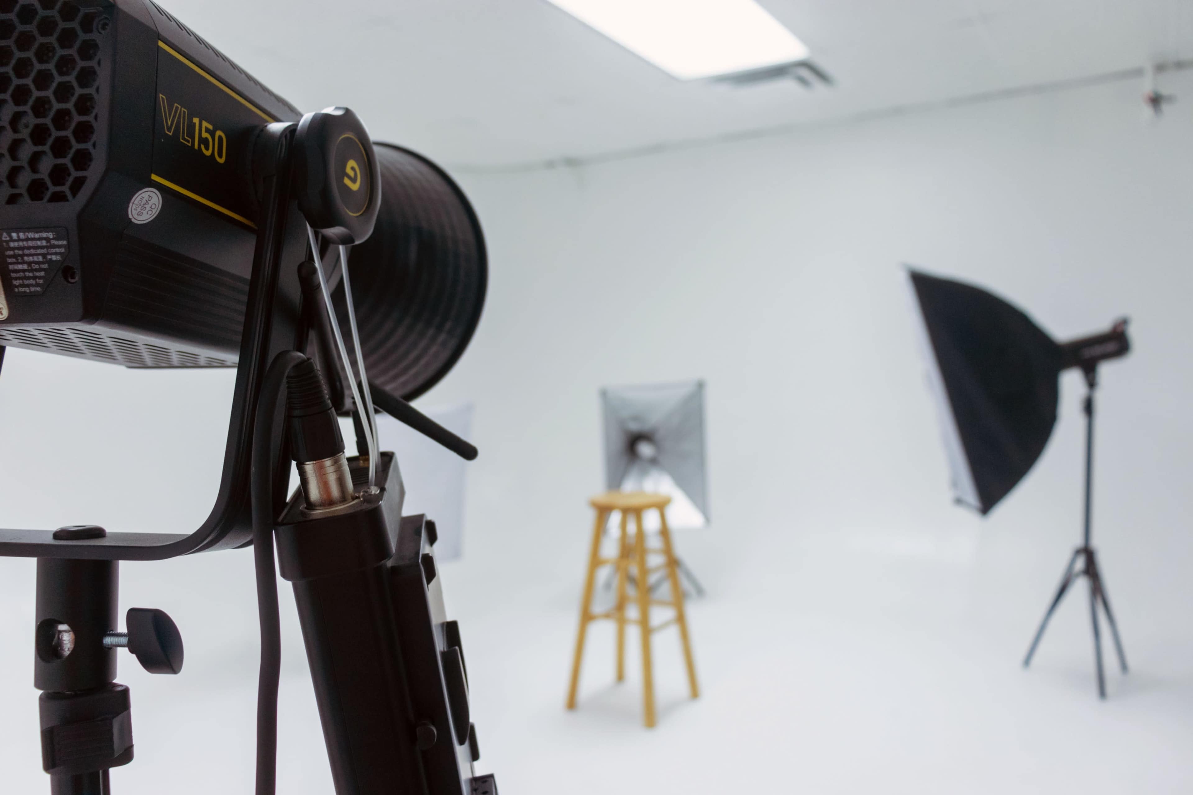 A photography studio is set up with a wooden stool and softbox lighting in a white backdrop environment.