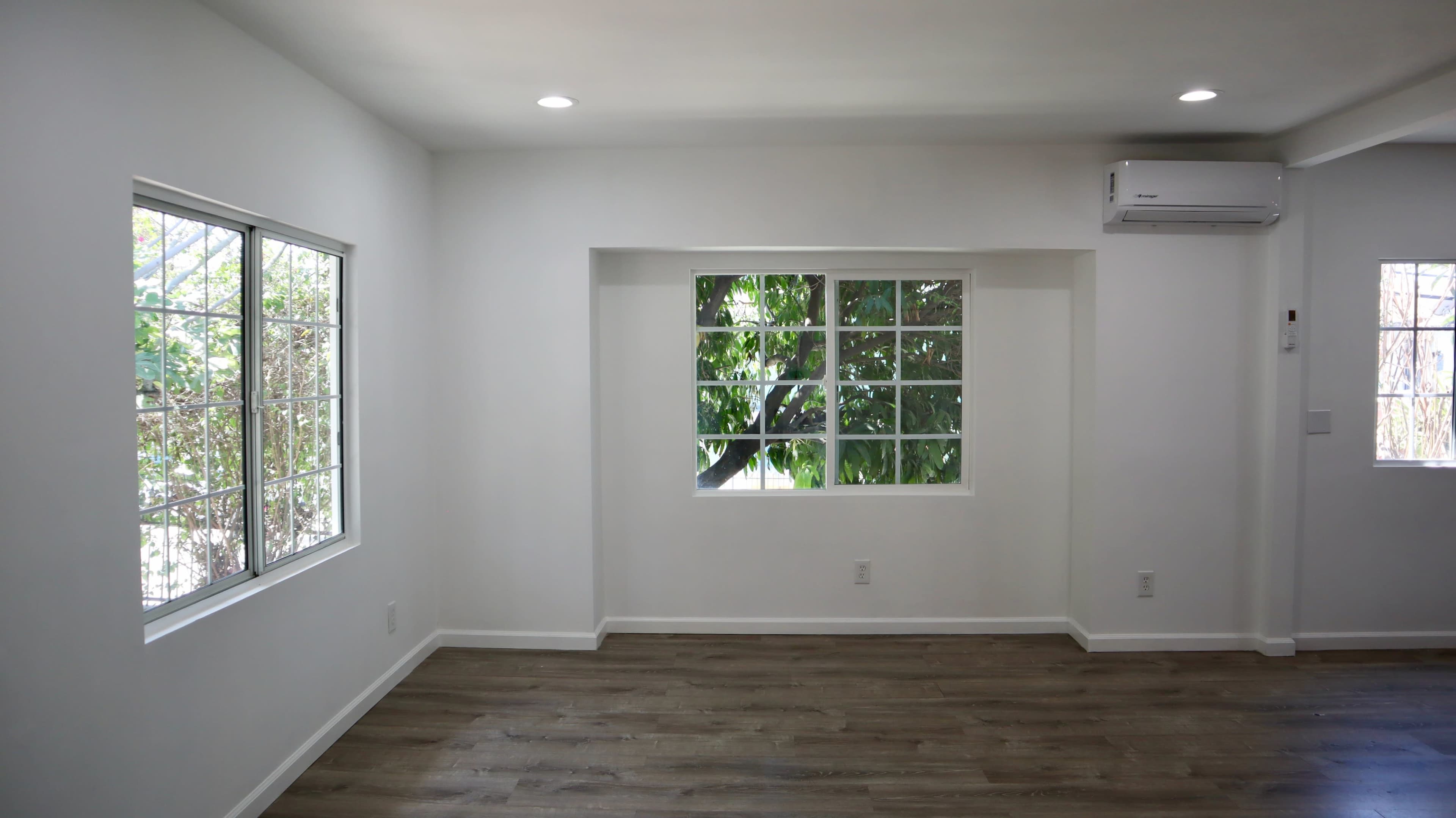 A well-lit interior space with two windows and light-colored walls, featuring wooden flooring.