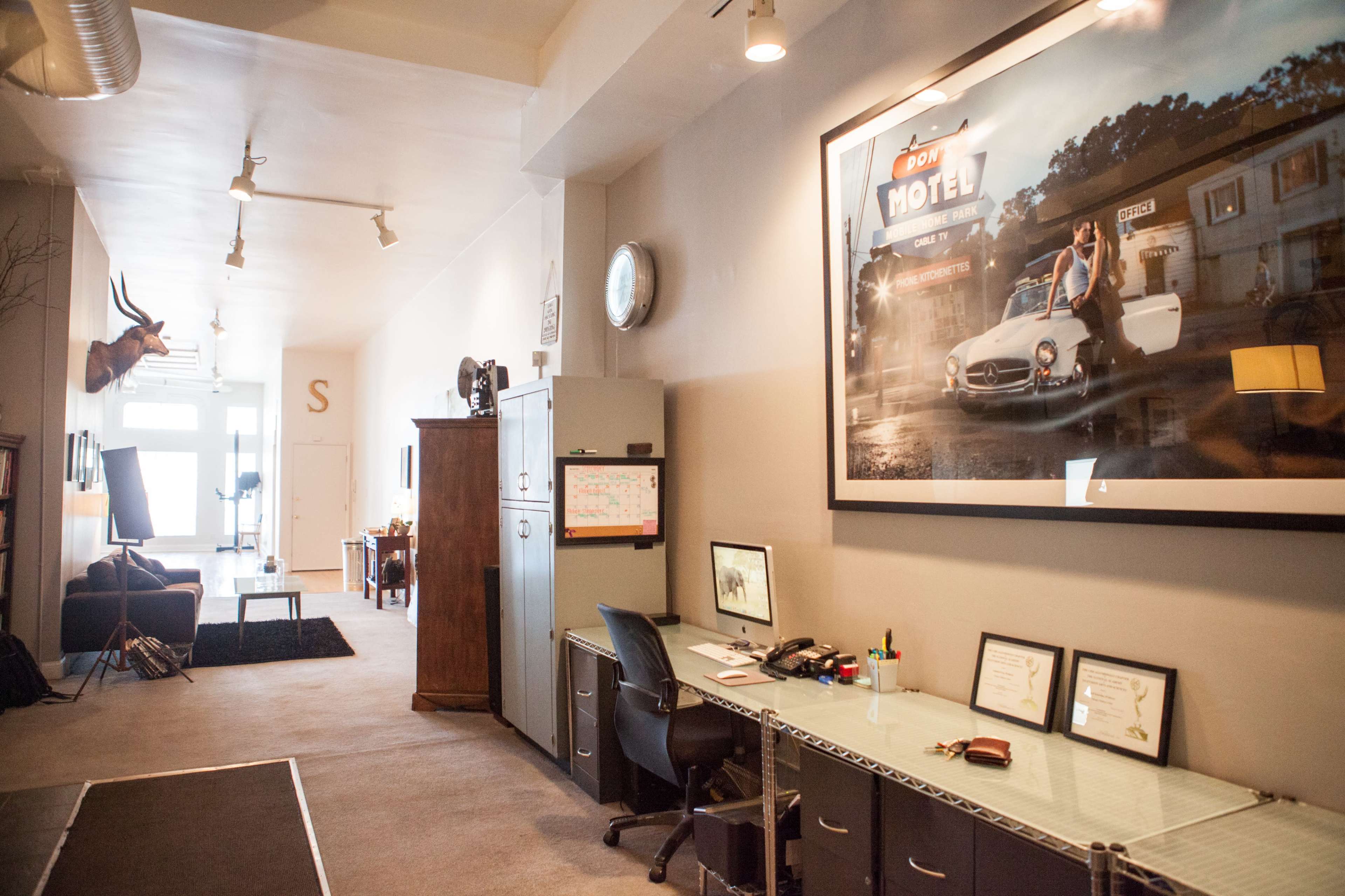The image shows a spacious office area with a desk, filing cabinet, and large framed photograph on the wall, alongside a cozy lounge area visible in the background.