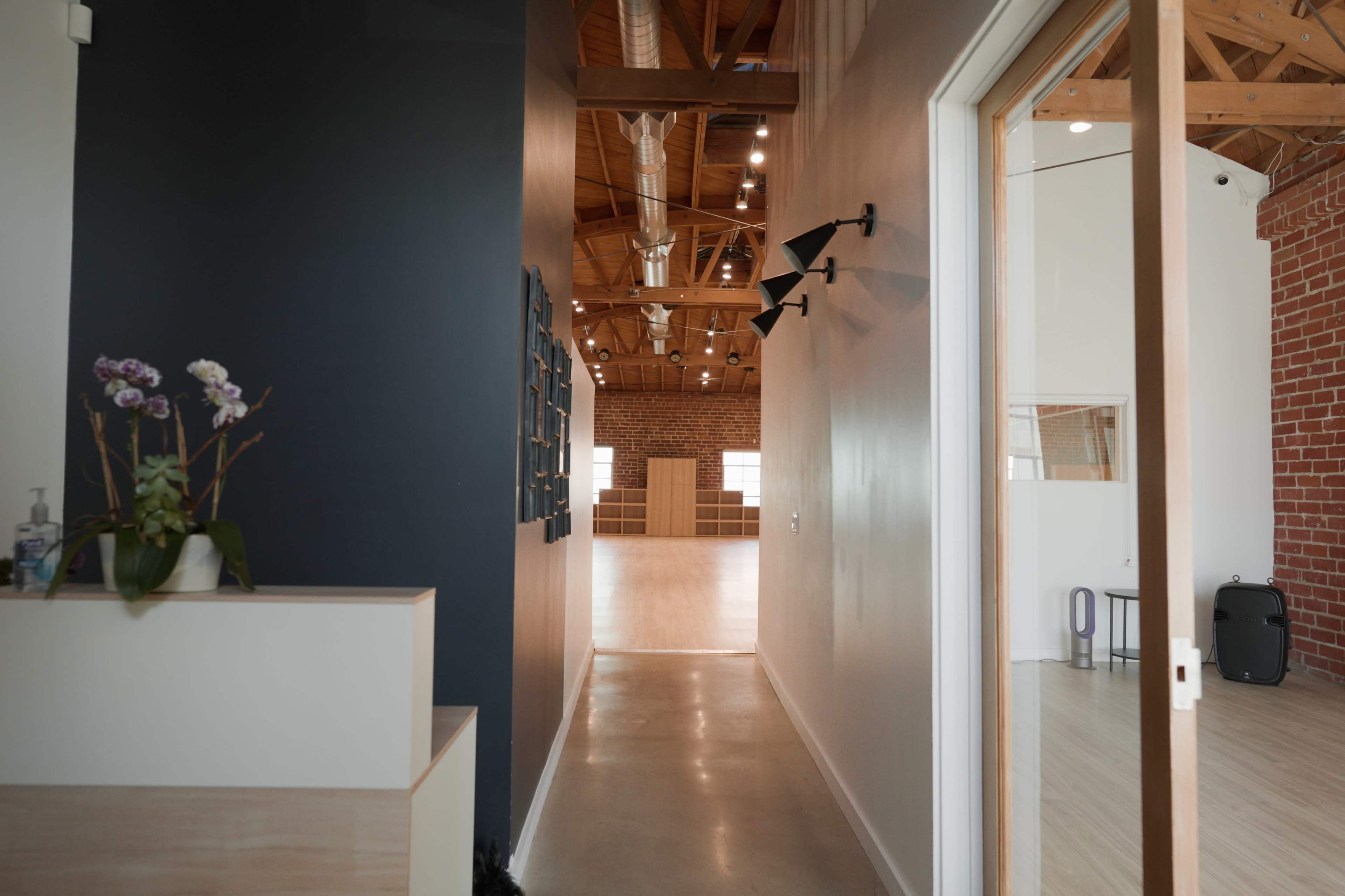 A well-lit hallway leads to a spacious, empty room with wooden beams and high ceilings.