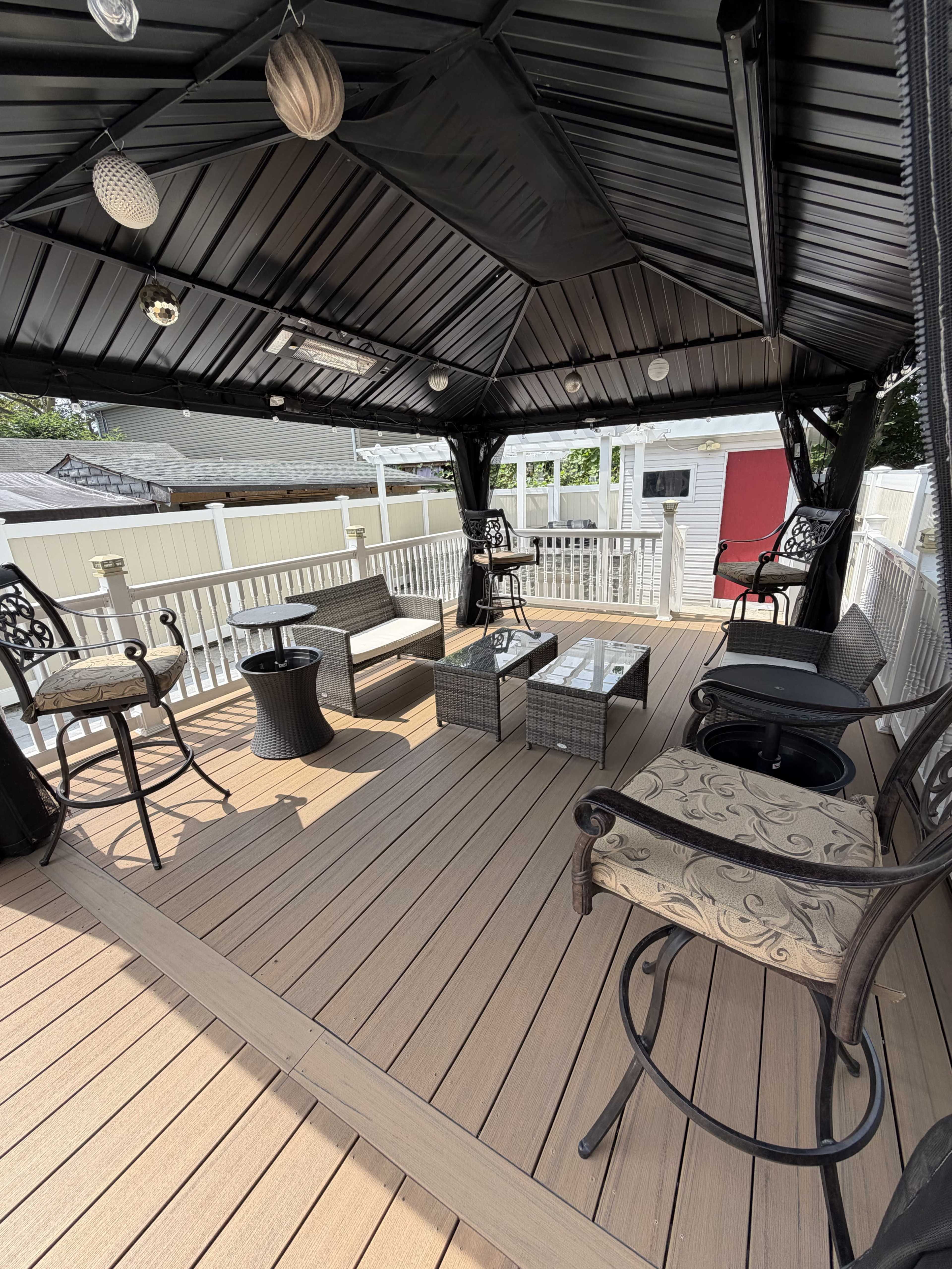 The image shows a covered outdoor seating area with several chairs, a table, and a decorative floor, all within a fenced space.
