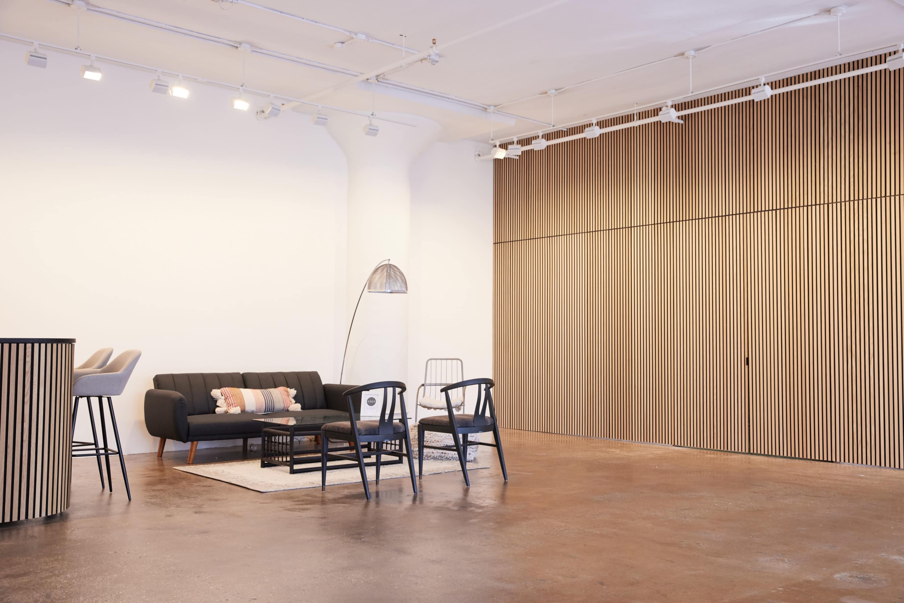 A modern interior space featuring a black sofa, several chairs, a floor lamp, and wooden wall paneling.