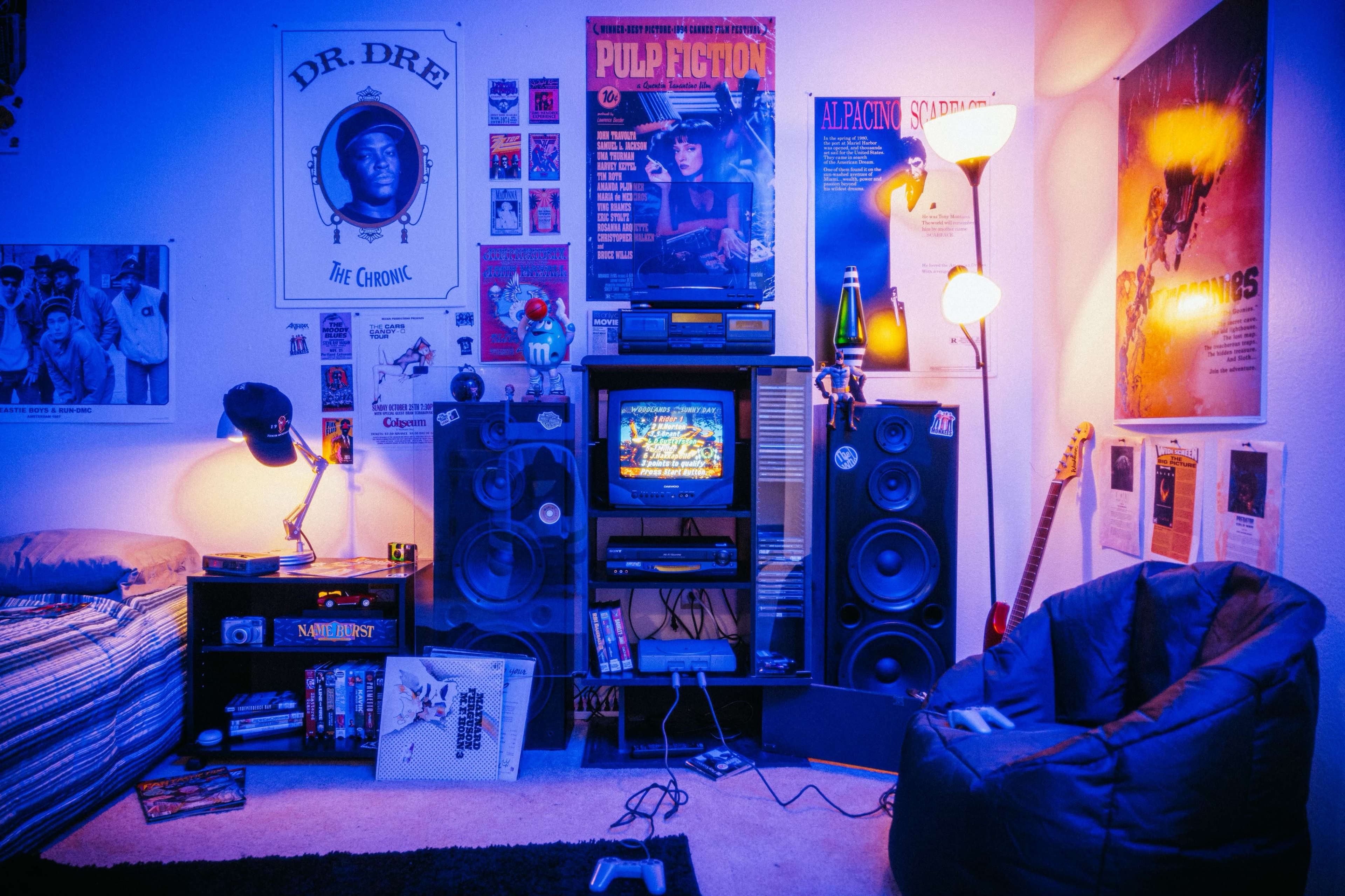 A colorful room with a bed, a TV stand featuring a classic television and speakers, and various movie posters and memorabilia on the walls.
