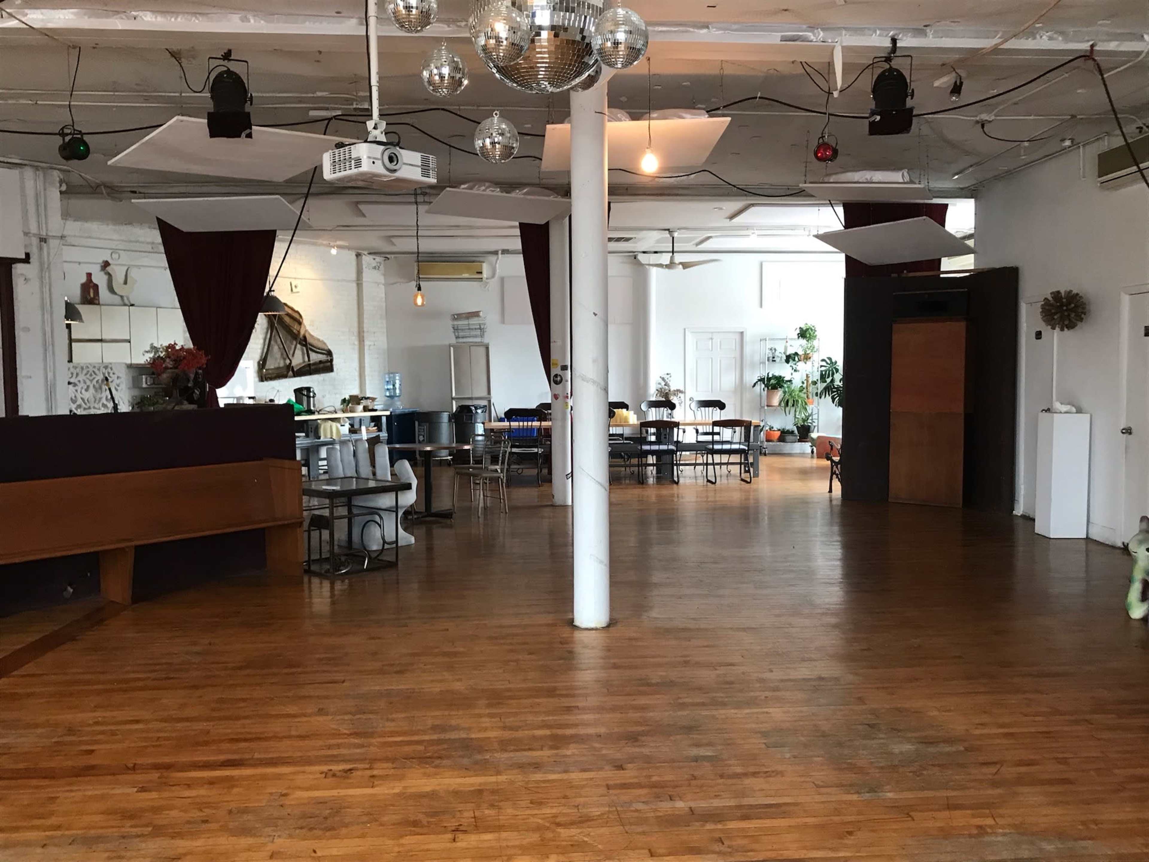 The image shows a spacious room with wooden floors and various tables, a bar area, and a large disco ball hanging from the ceiling.