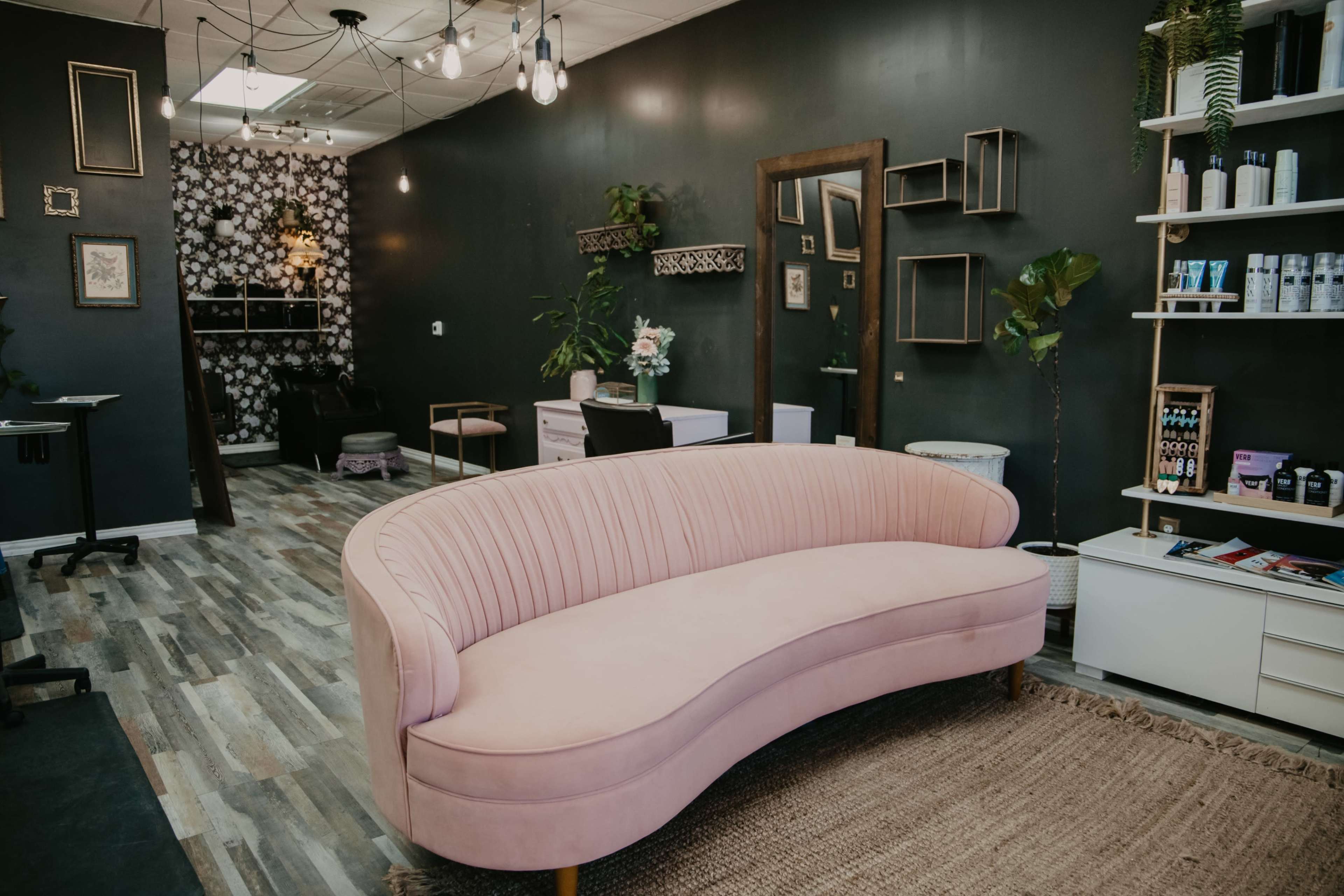 A stylish salon interior featuring a pink curved sofa, patterned wallpaper, and shelves filled with beauty products.