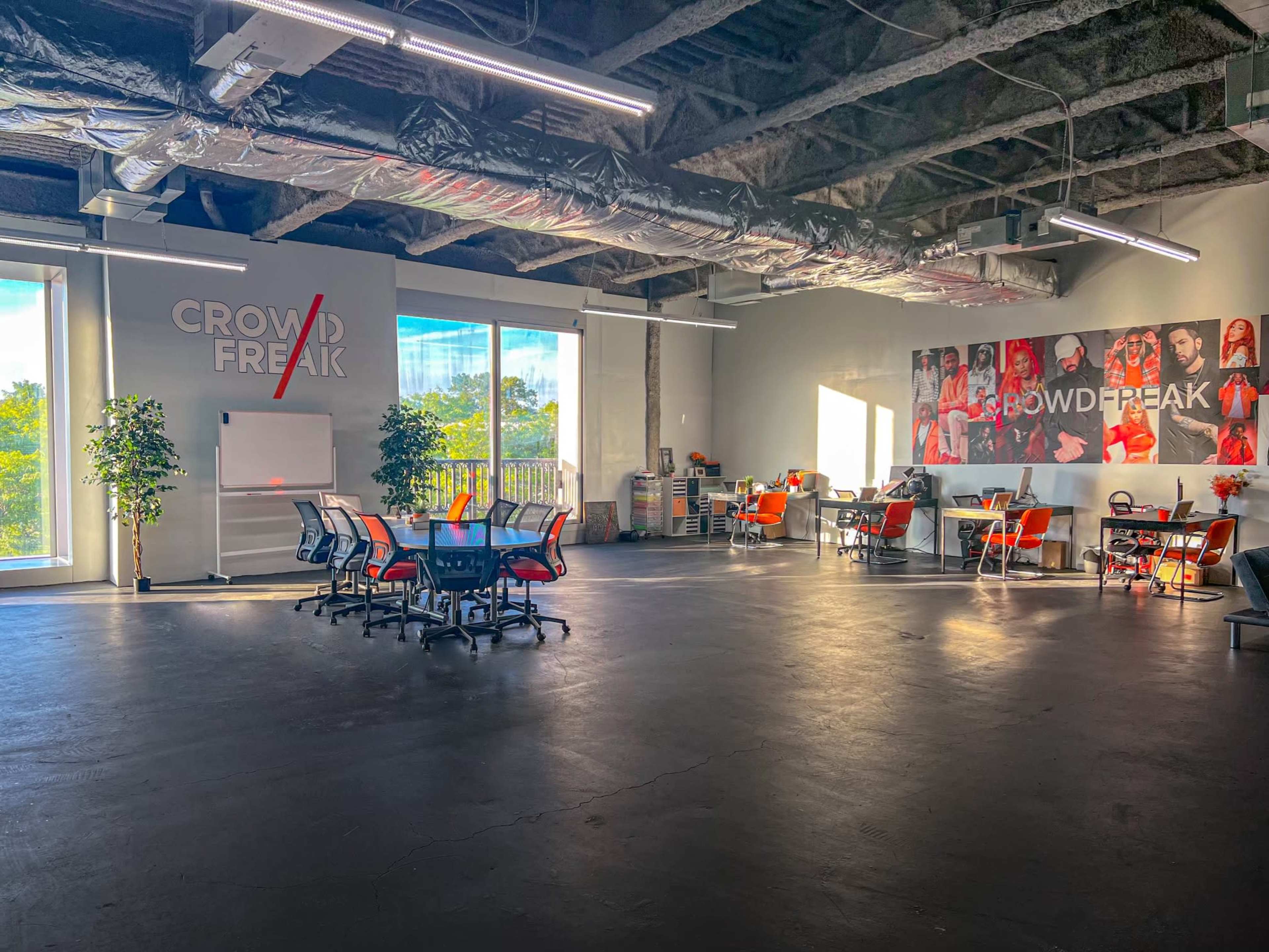 A spacious office interior with modern furniture, large windows, and a branded wall featuring multiple images.