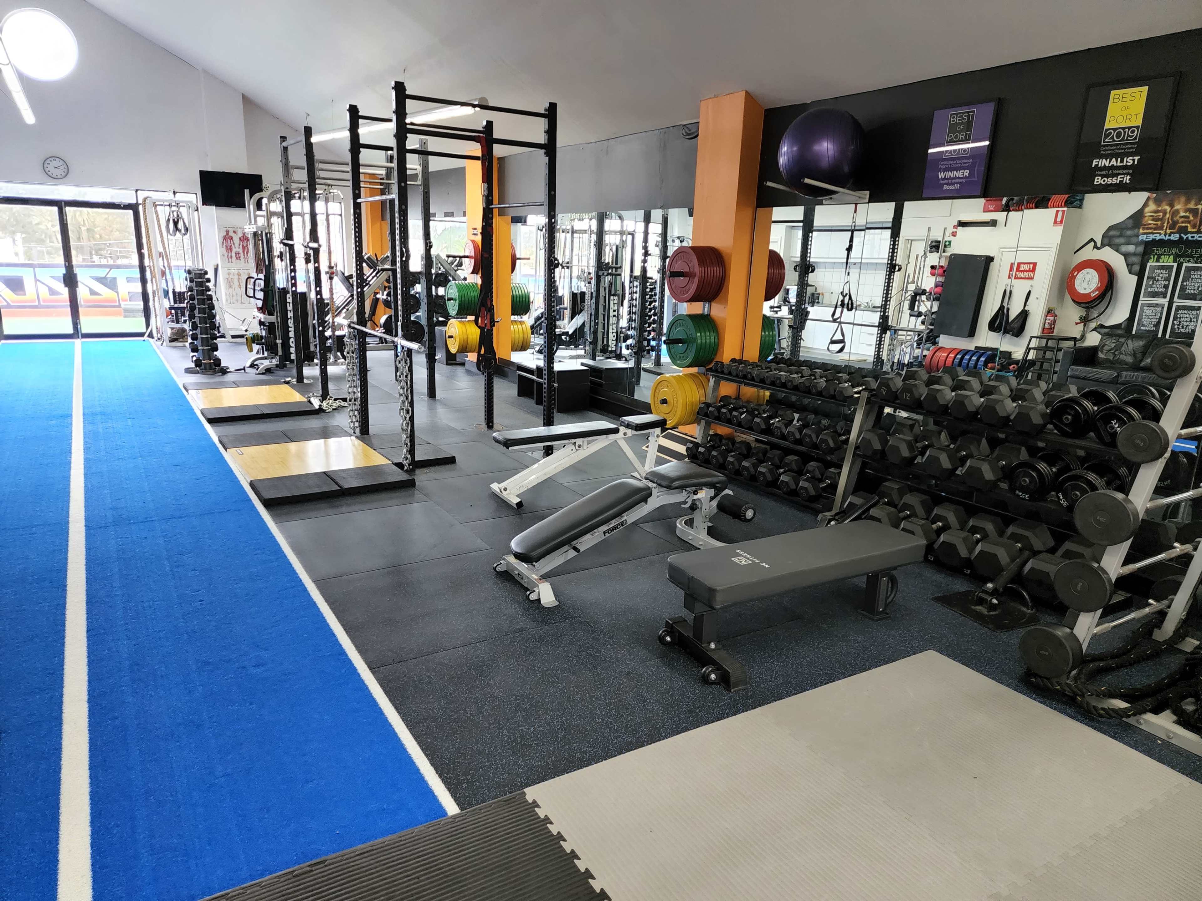 A gym interior with weightlifting equipment, benches, and free weights arranged on racks along one side of the room.