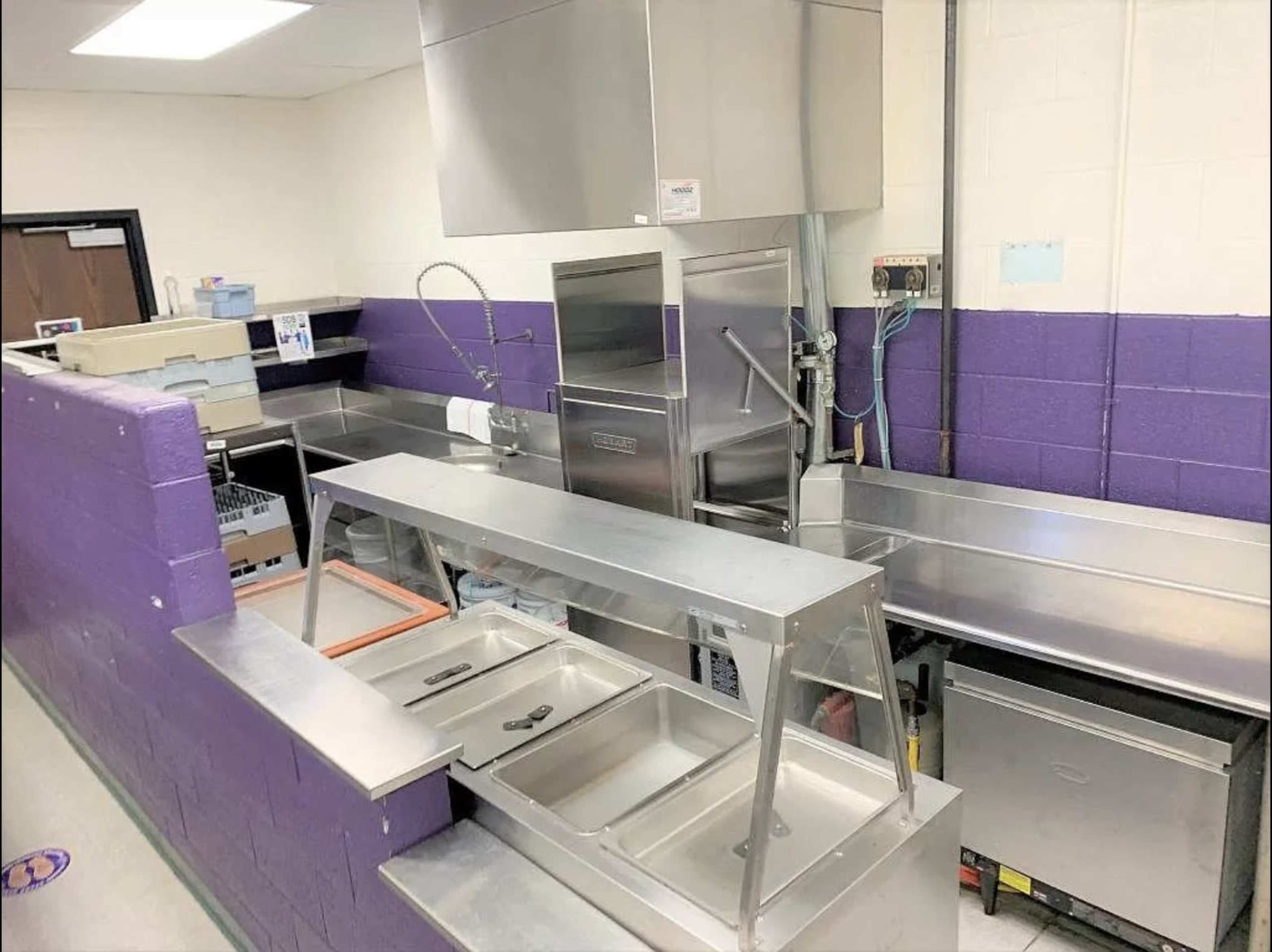 The image shows a stainless steel kitchen area with multiple countertop sections and a commercial sink.