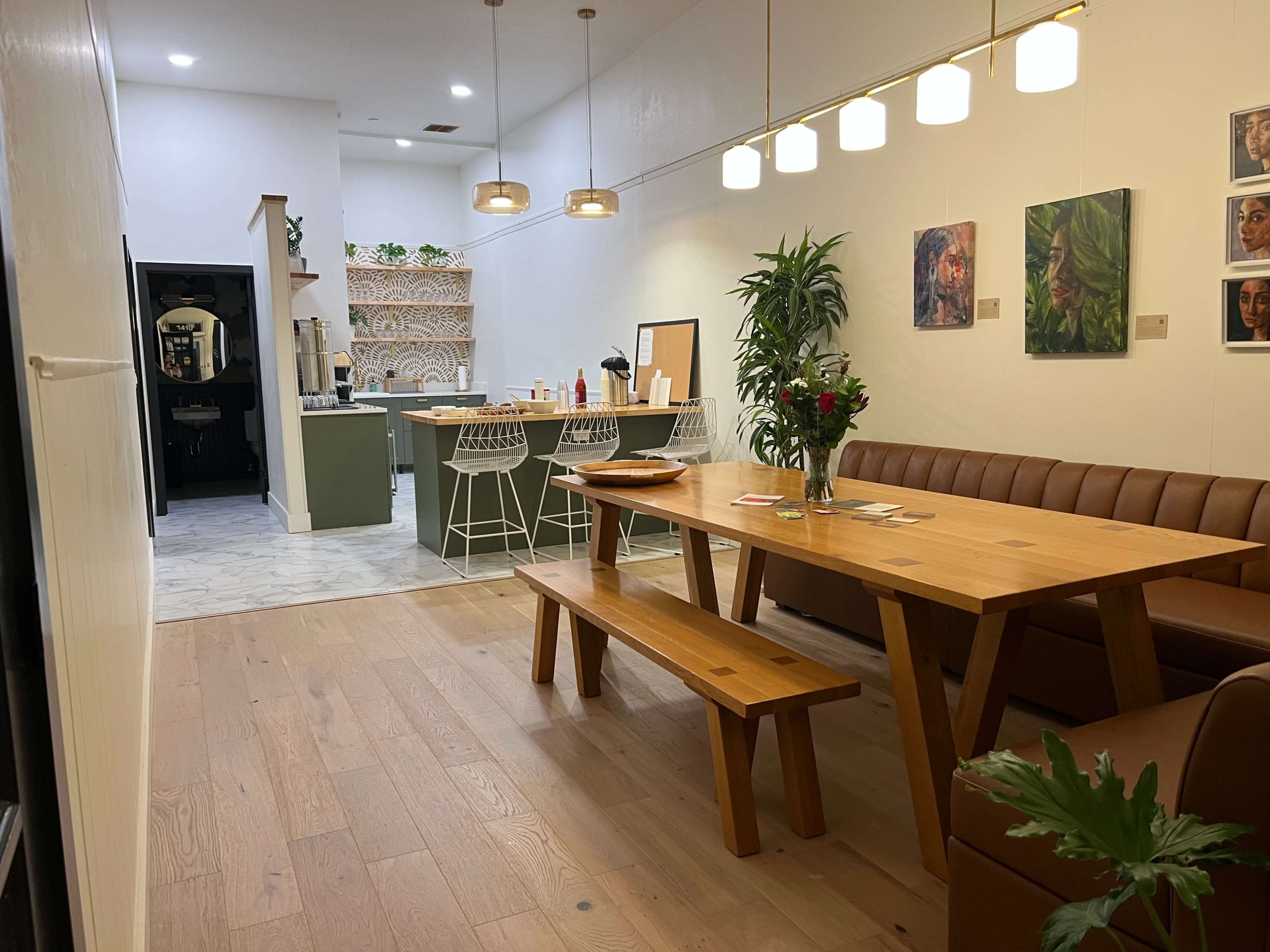 A dining area with a wooden table and benches is adjacent to a kitchen bar with high stools, featuring modern decor and plants.
