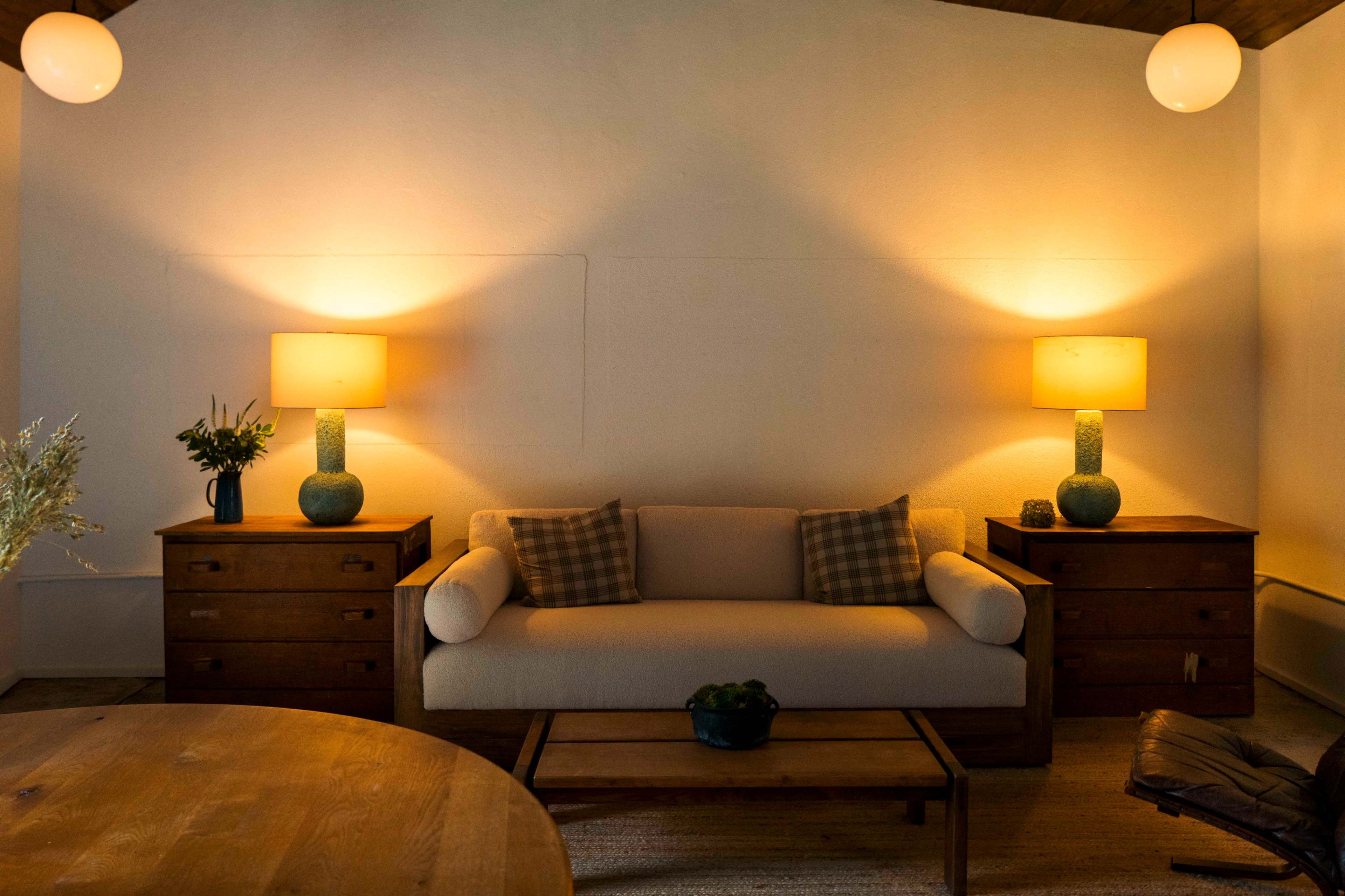The image shows a cozy living room with a beige sofa, two wooden side tables with lamps, and warm lighting creating a relaxed atmosphere.