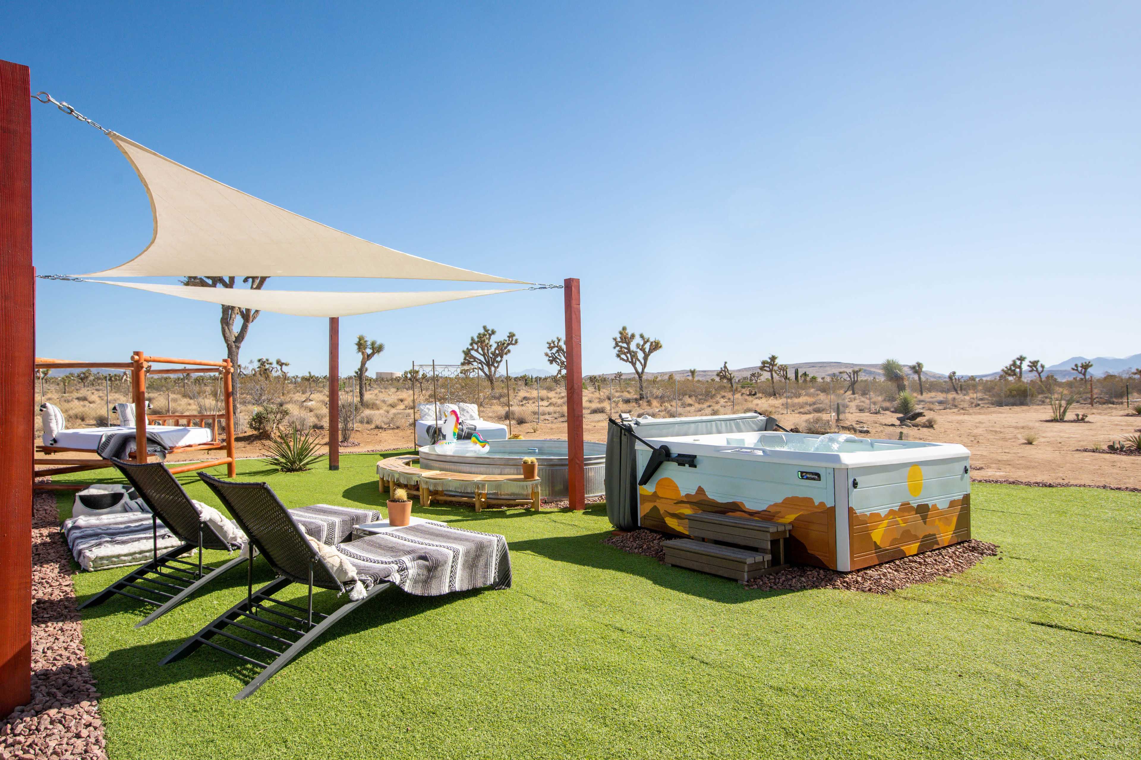 The image shows a hot tub and a circular bathtub surrounded by lounge chairs and a shaded area in a desert landscape.