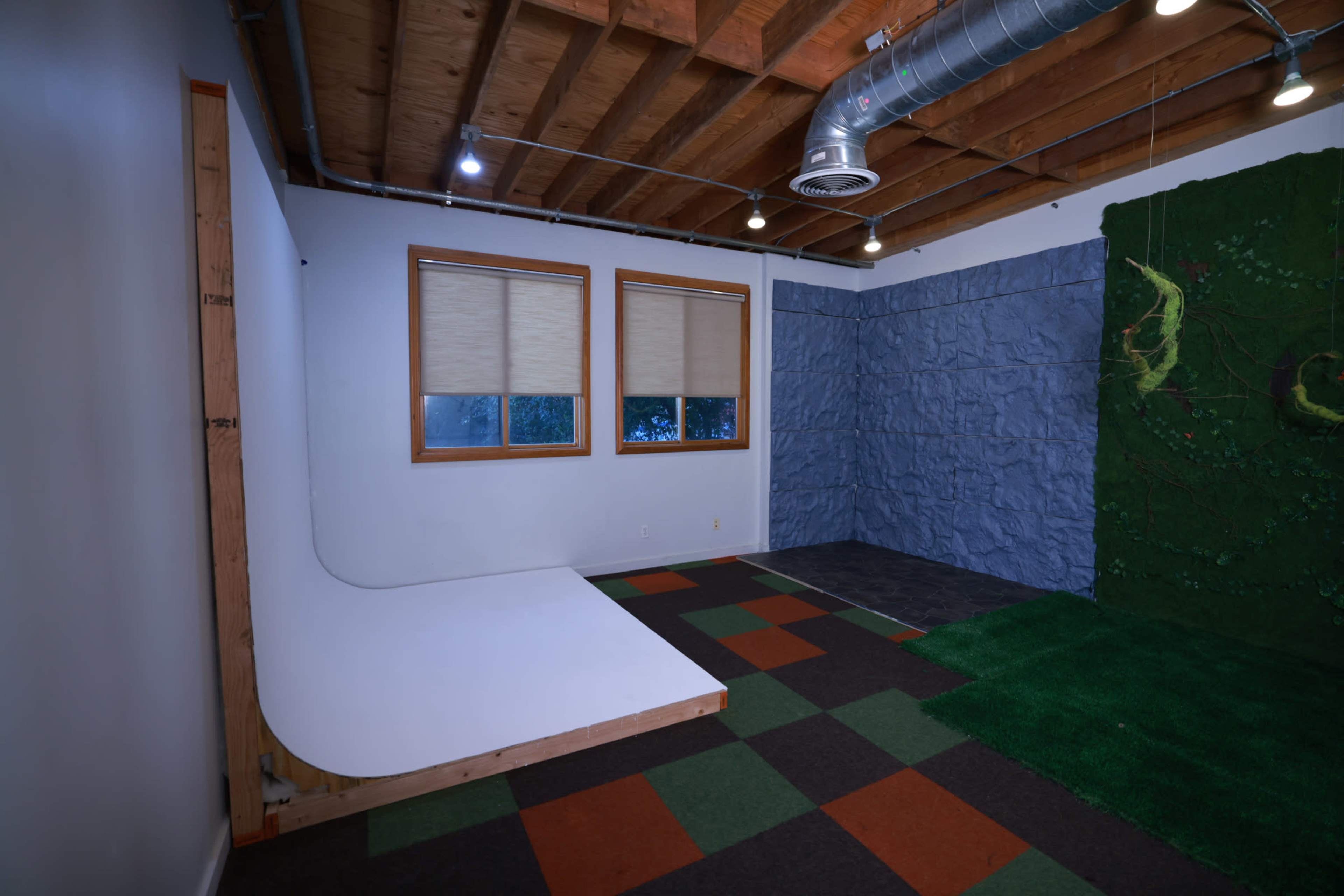 The image shows a spacious indoor studio featuring a white backdrop area, a textured stone wall, and a green grass-like floor section.