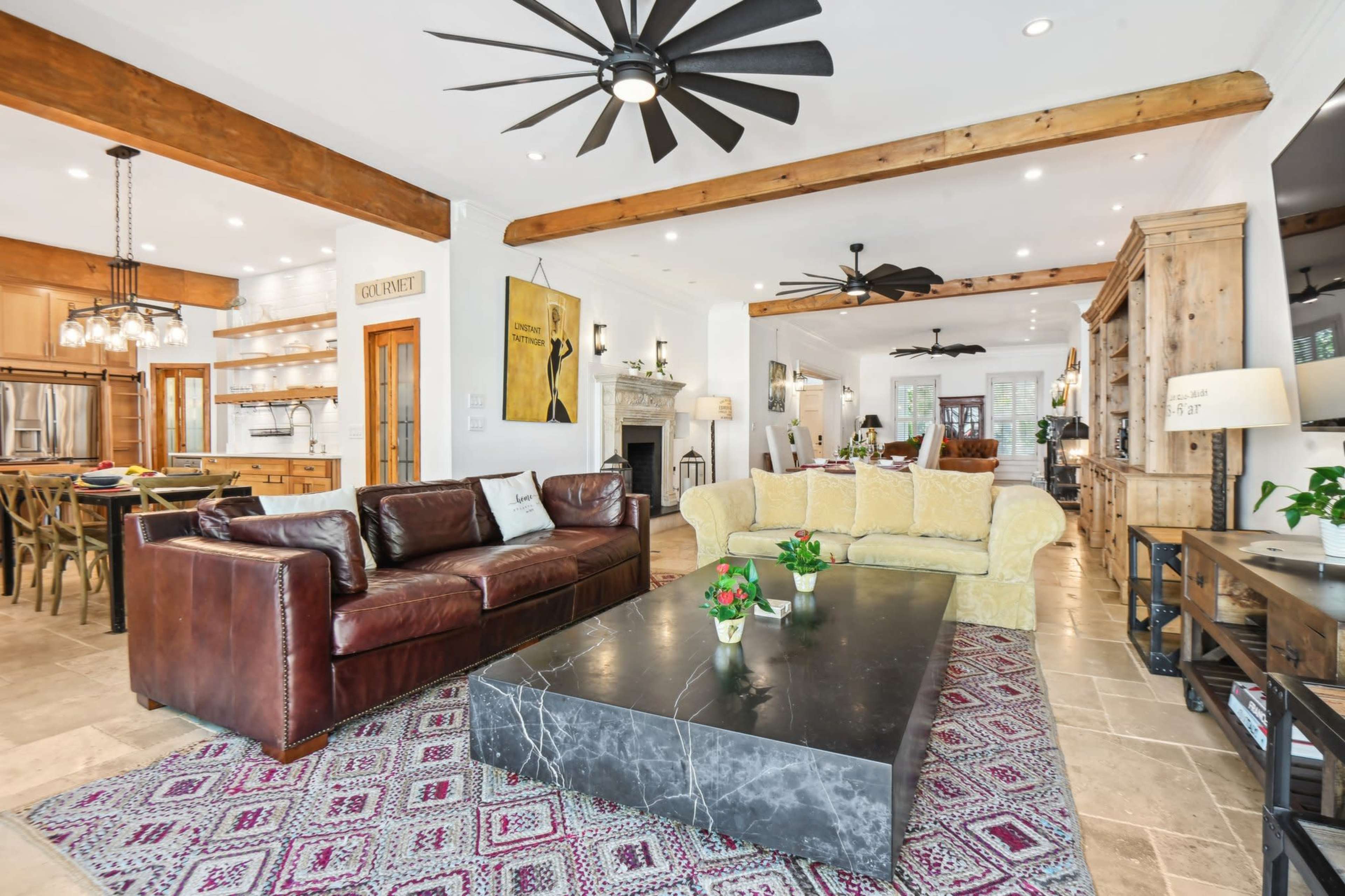 The image shows a spacious living area with a leather sofa, a yellow couch, a large coffee table, and exposed wooden beams, creating an inviting atmosphere.