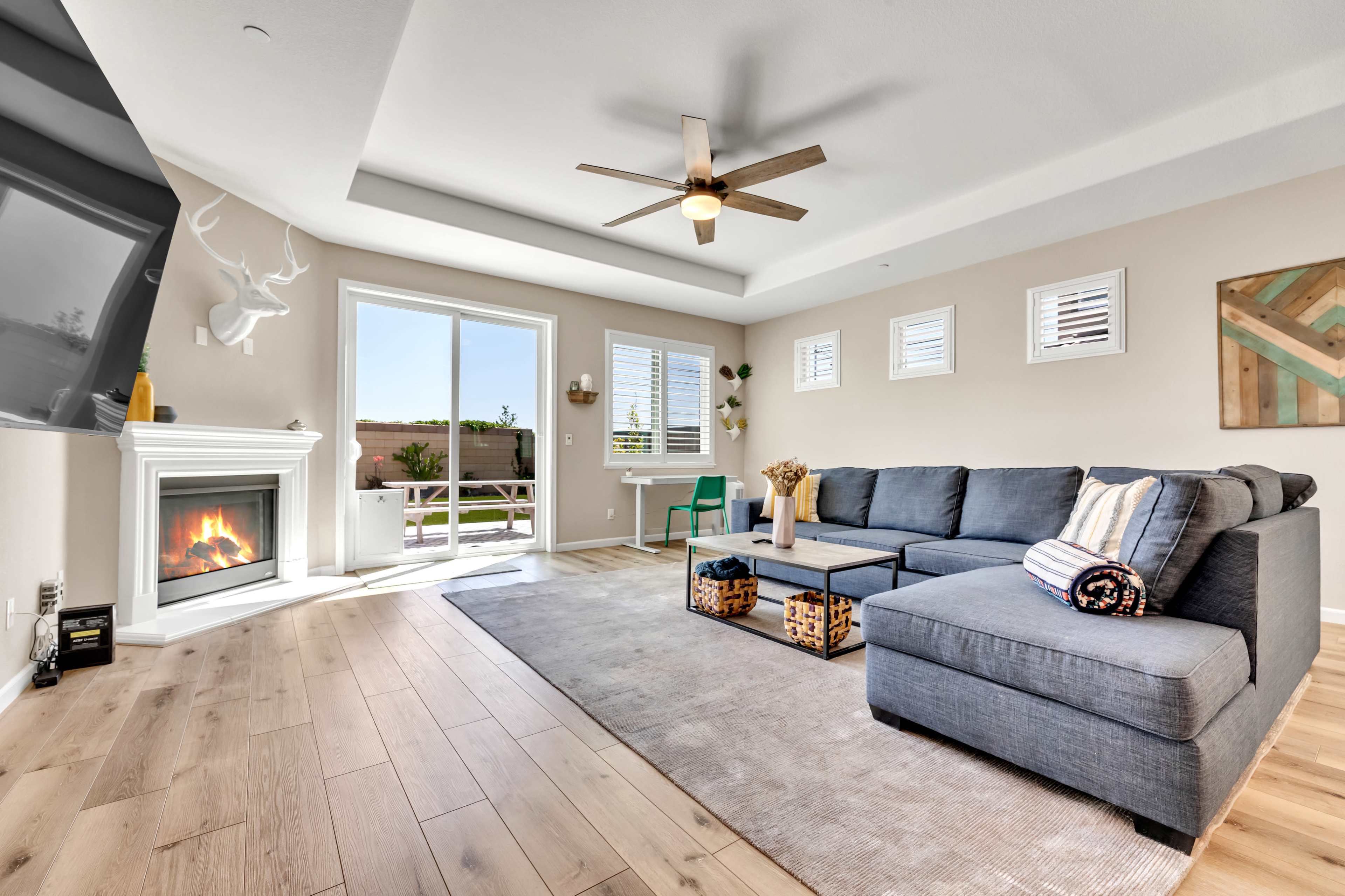 A modern living room with a gray sectional sofa, a fireplace, and large windows allowing natural light to enter.