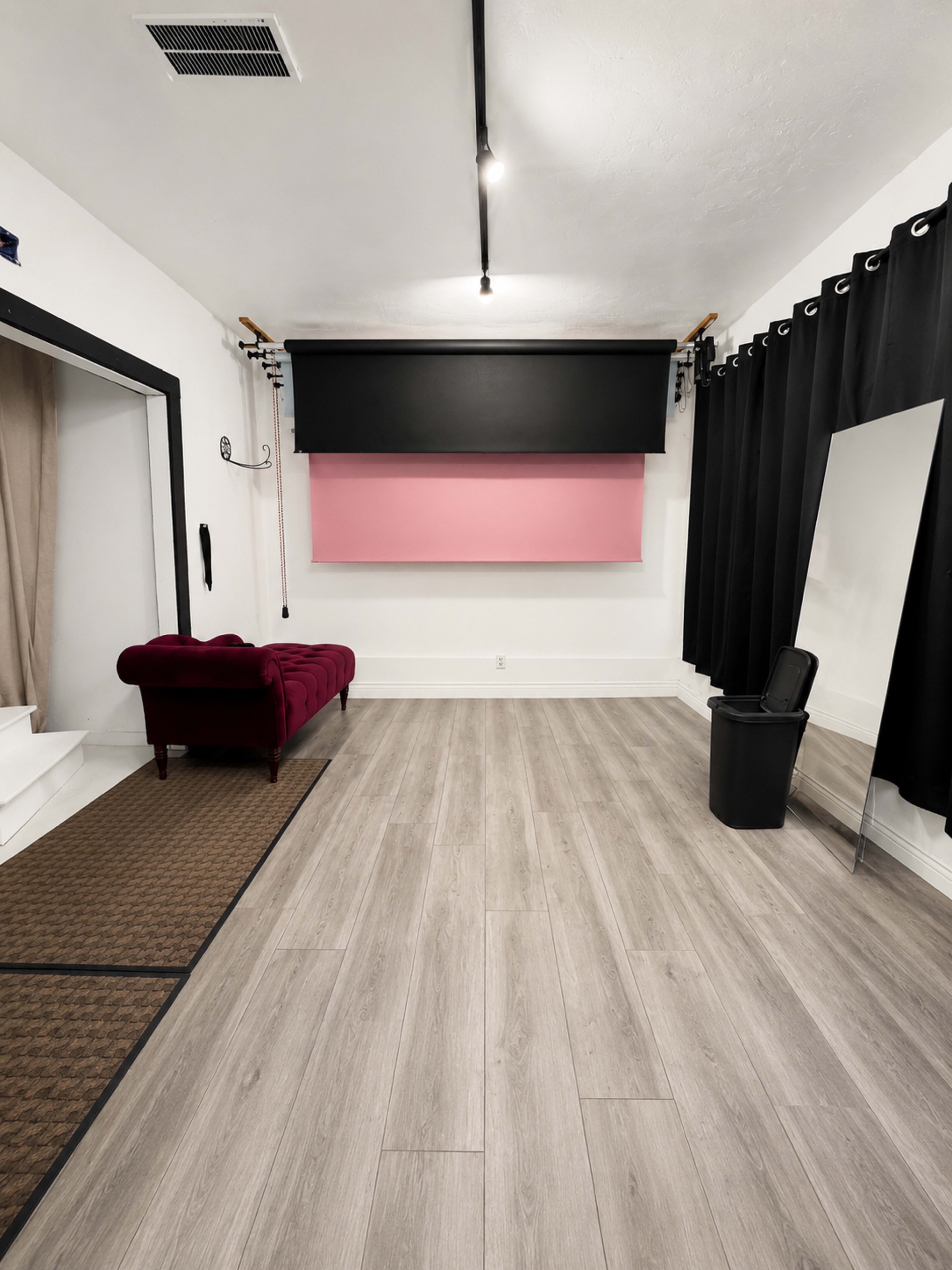 The image shows an empty studio or room with a red couch, a large pink and black backdrop, and a mirror along one wall.