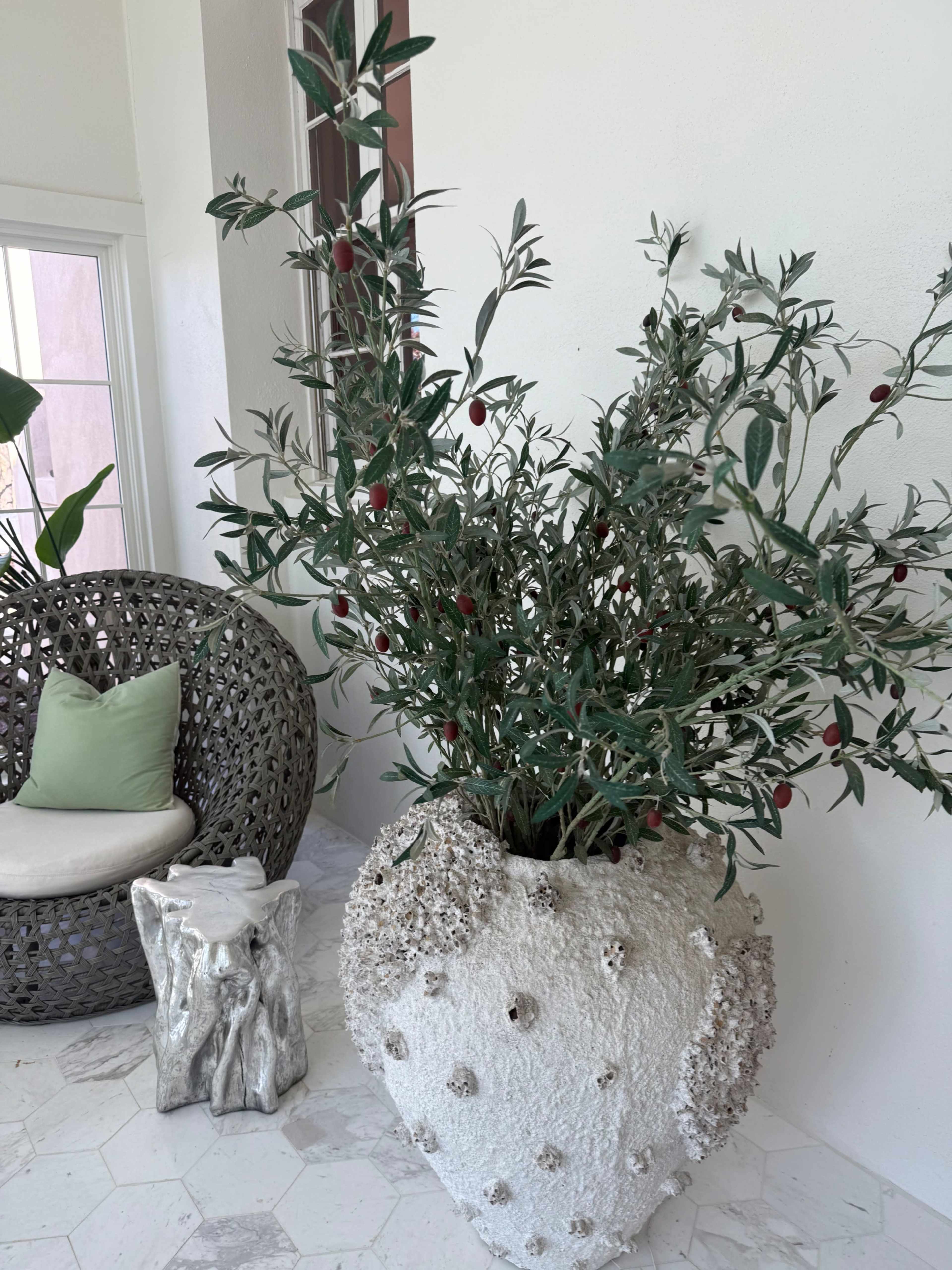 A large decorative vase filled with greenery and red berries stands next to a textured chair on a tiled floor.
