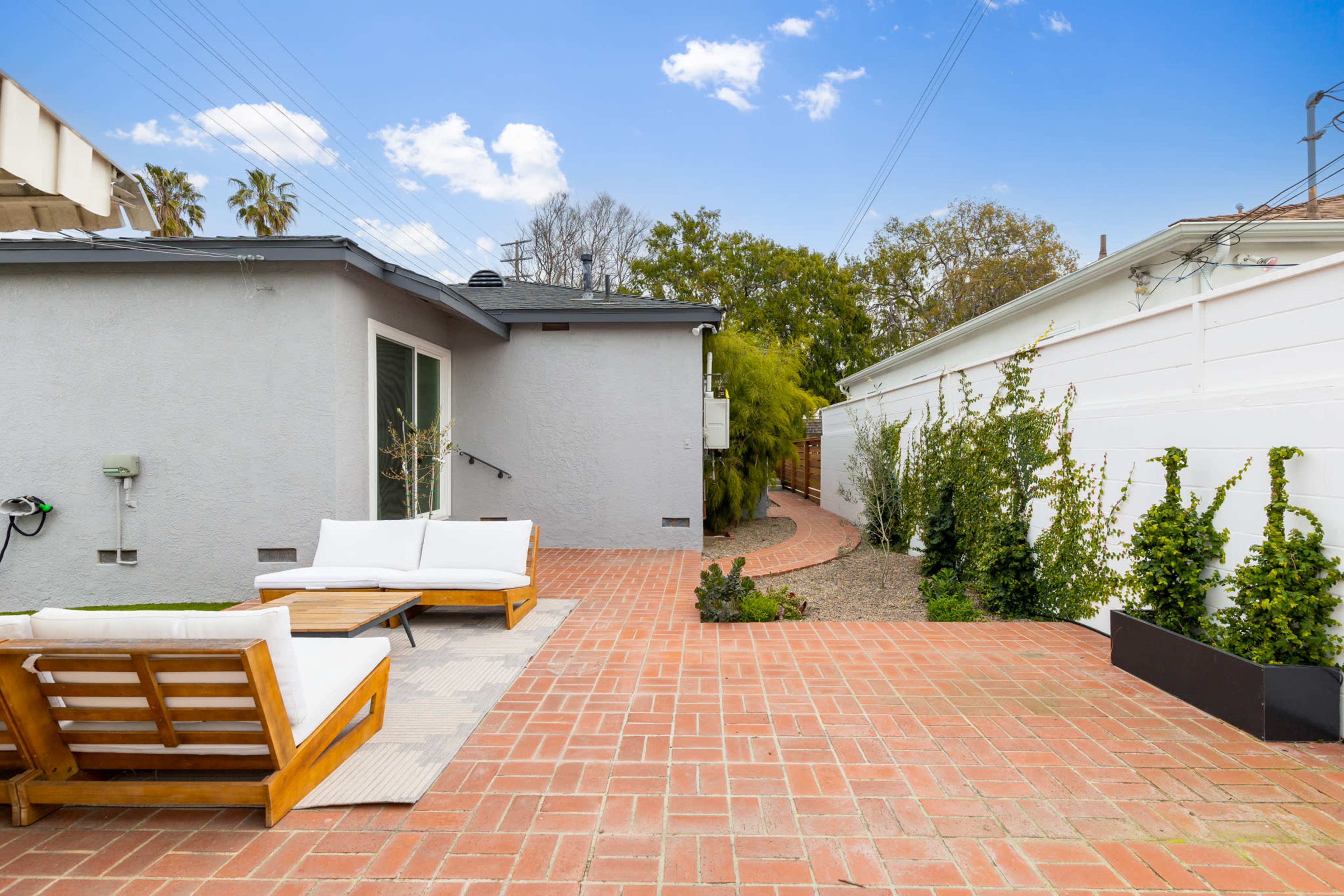 A paved outdoor patio area with wooden furniture and a pathway leading to a garden space.