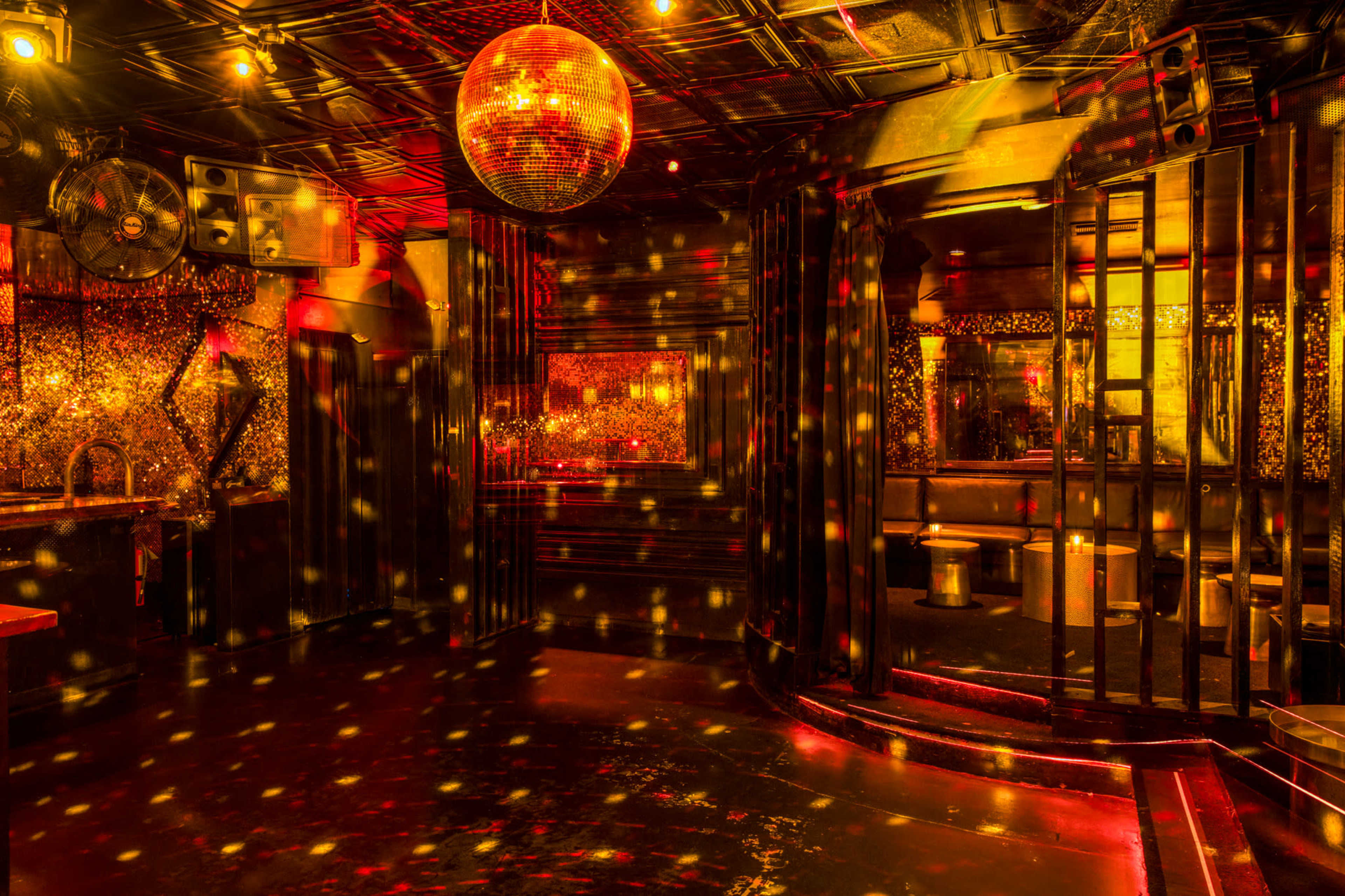 The interior of a dimly lit nightclub features a disco ball reflecting colorful lights onto the walls and floor.