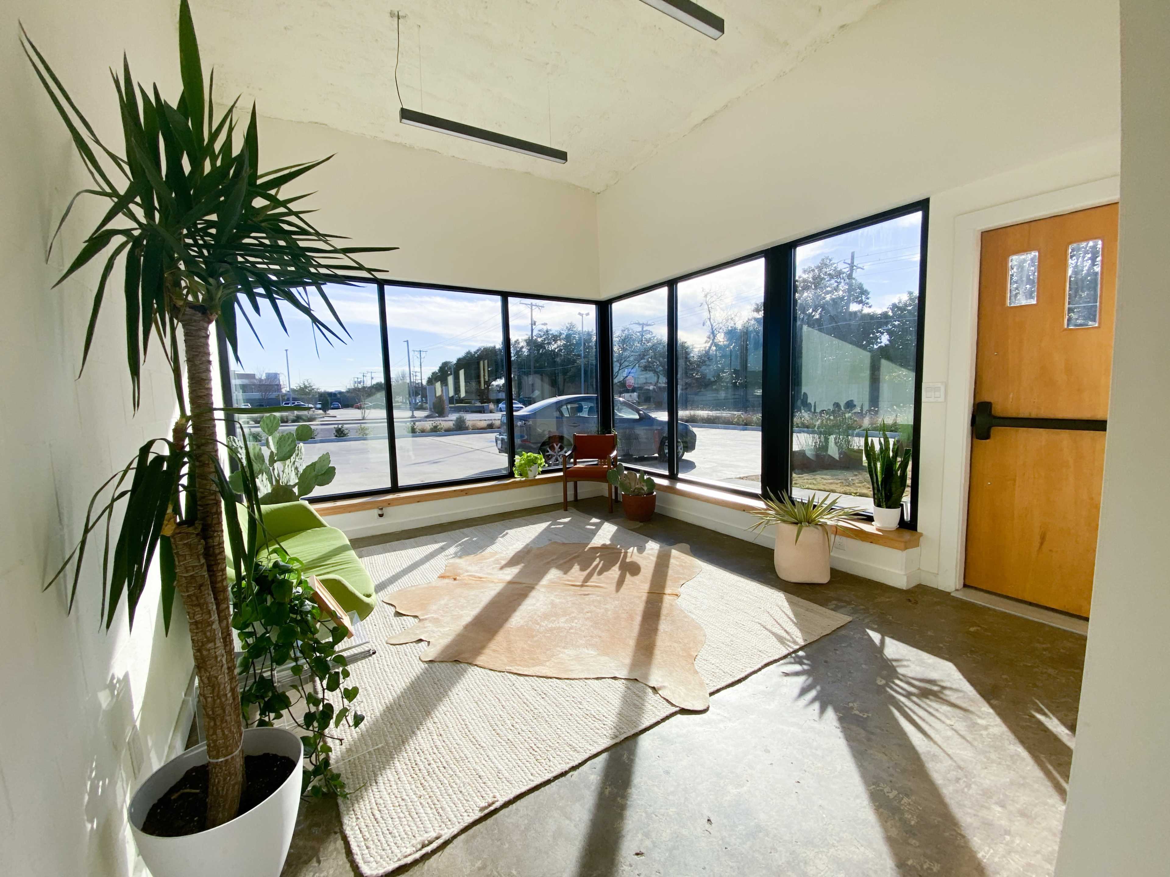 A bright, minimalist foyer with large windows, a potted palm, a cowhide rug, and a small armchair.