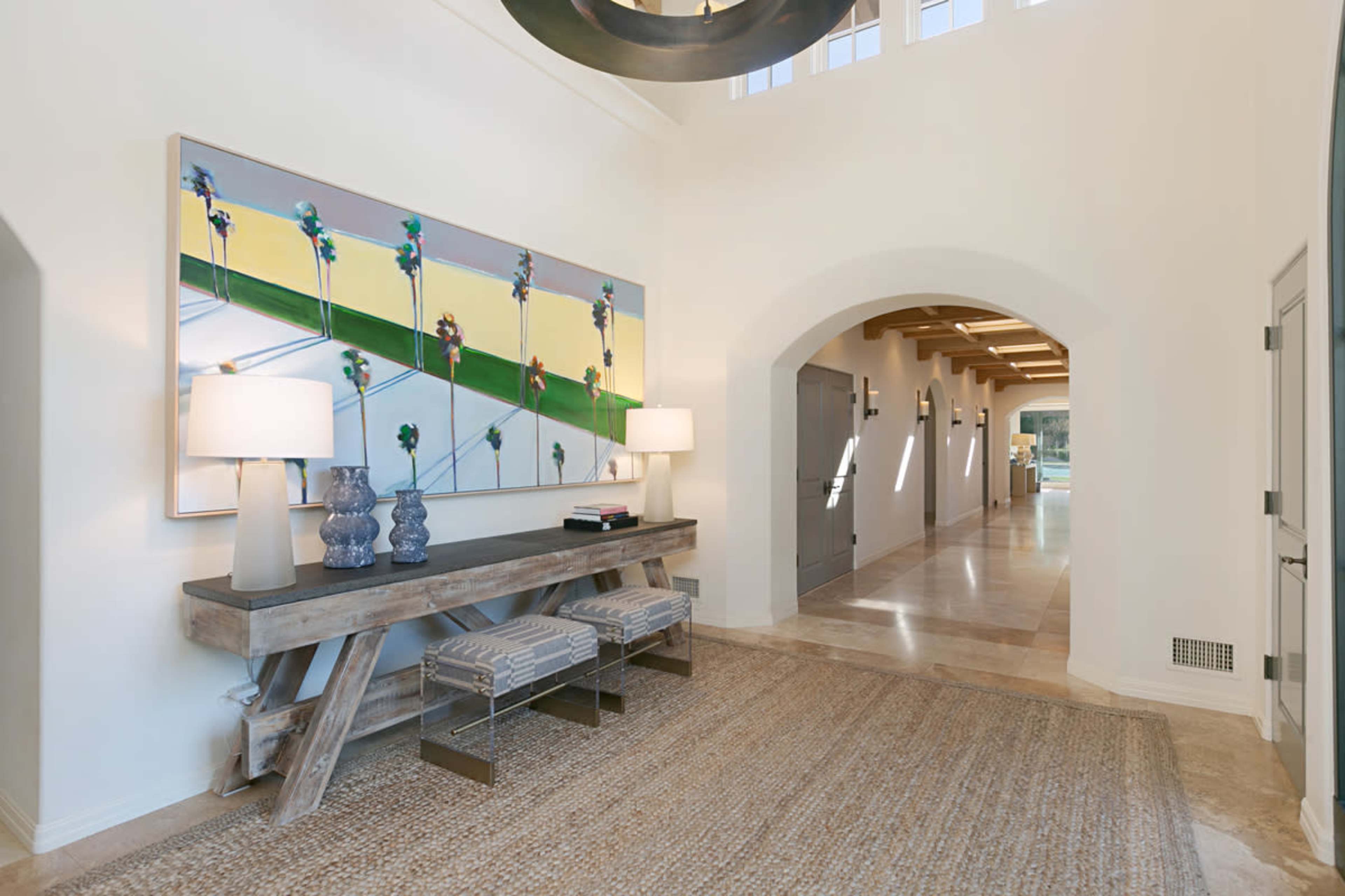 A well-lit hallway with a modern console table, two lamps, and a large artwork on the wall.