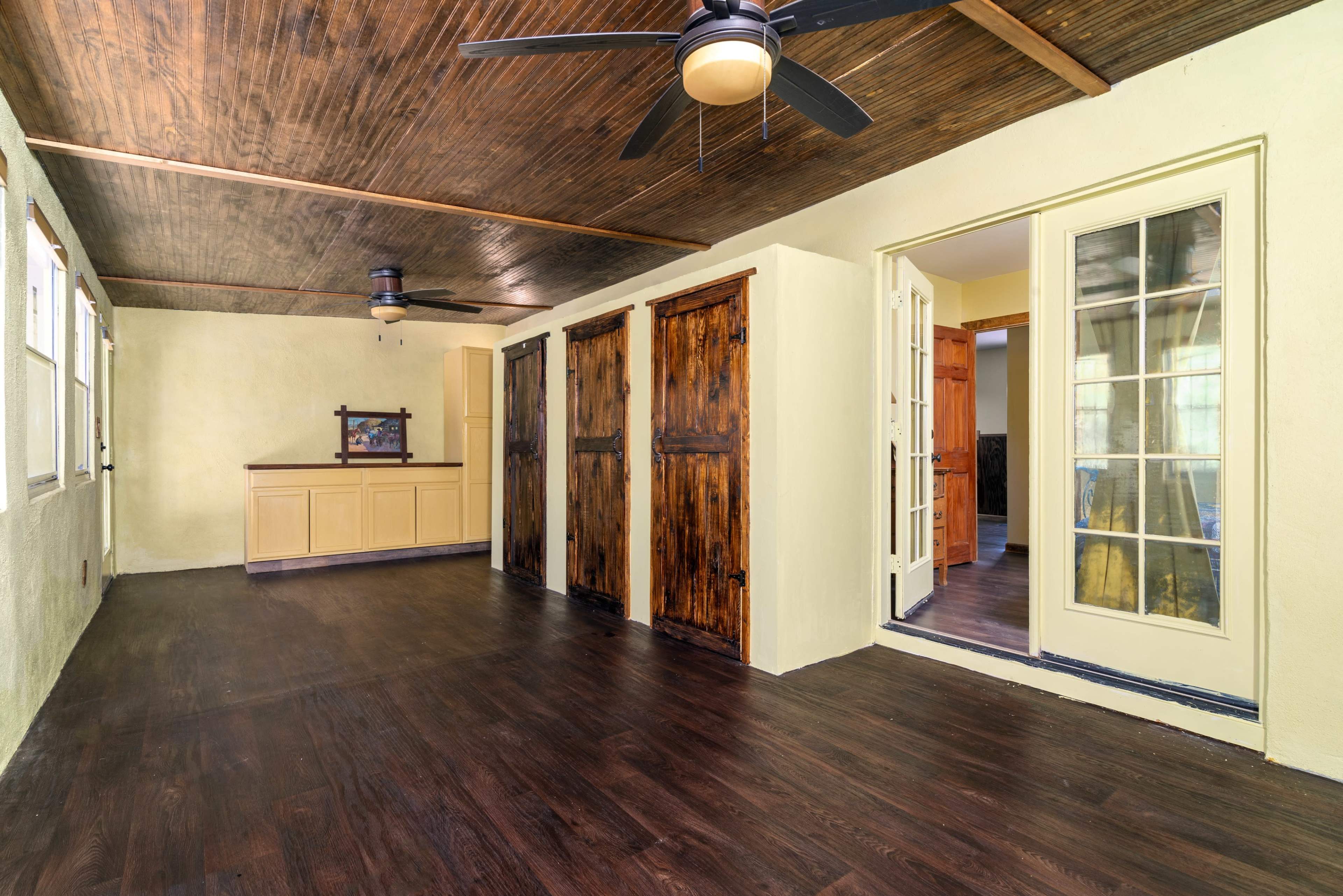 The image shows a spacious room with a wooden ceiling, dark wood flooring, and several closed wooden doors along one wall.