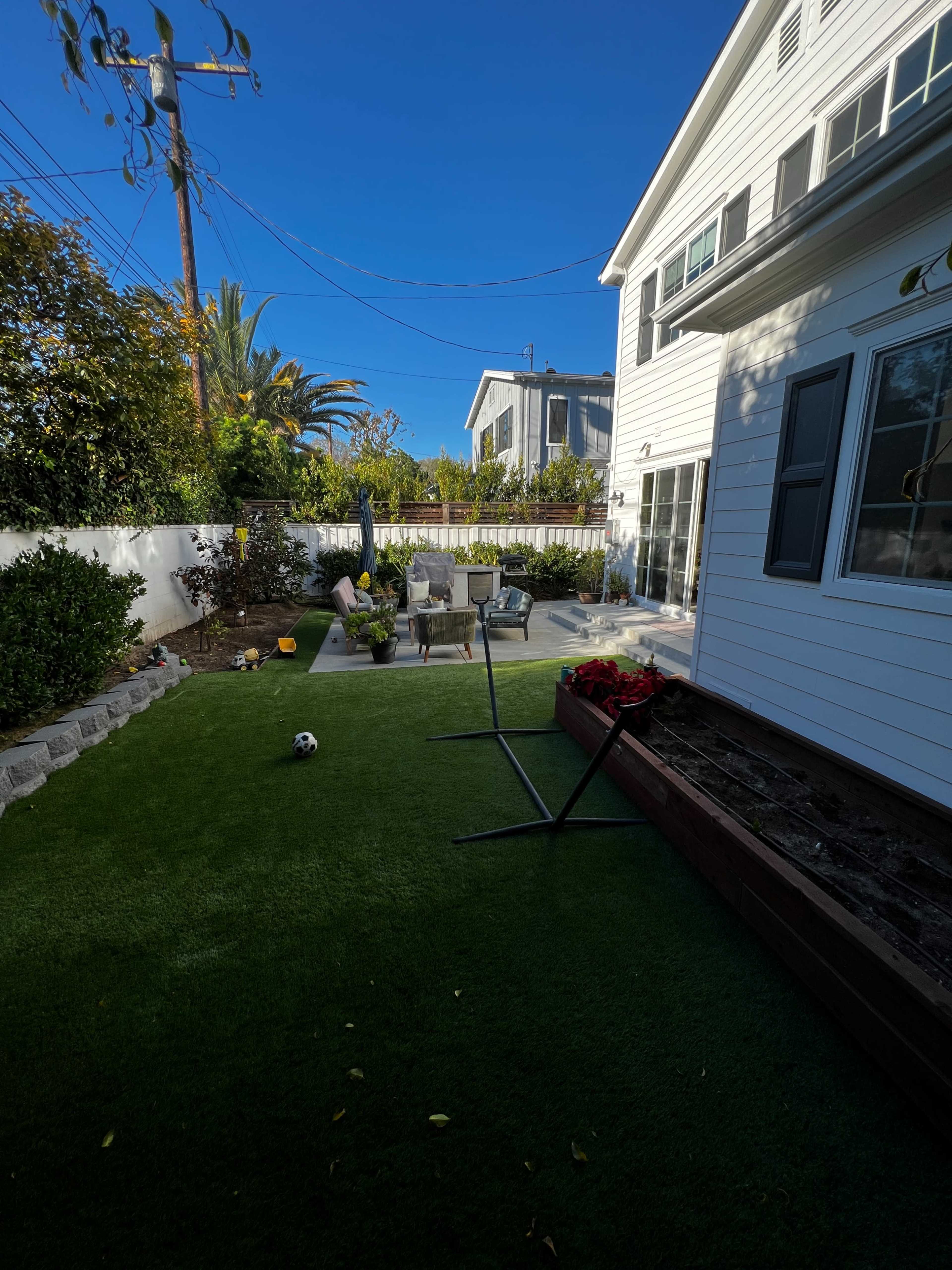 A backyard with artificial grass, a patio area with chairs and a table, and a small soccer ball on the ground.