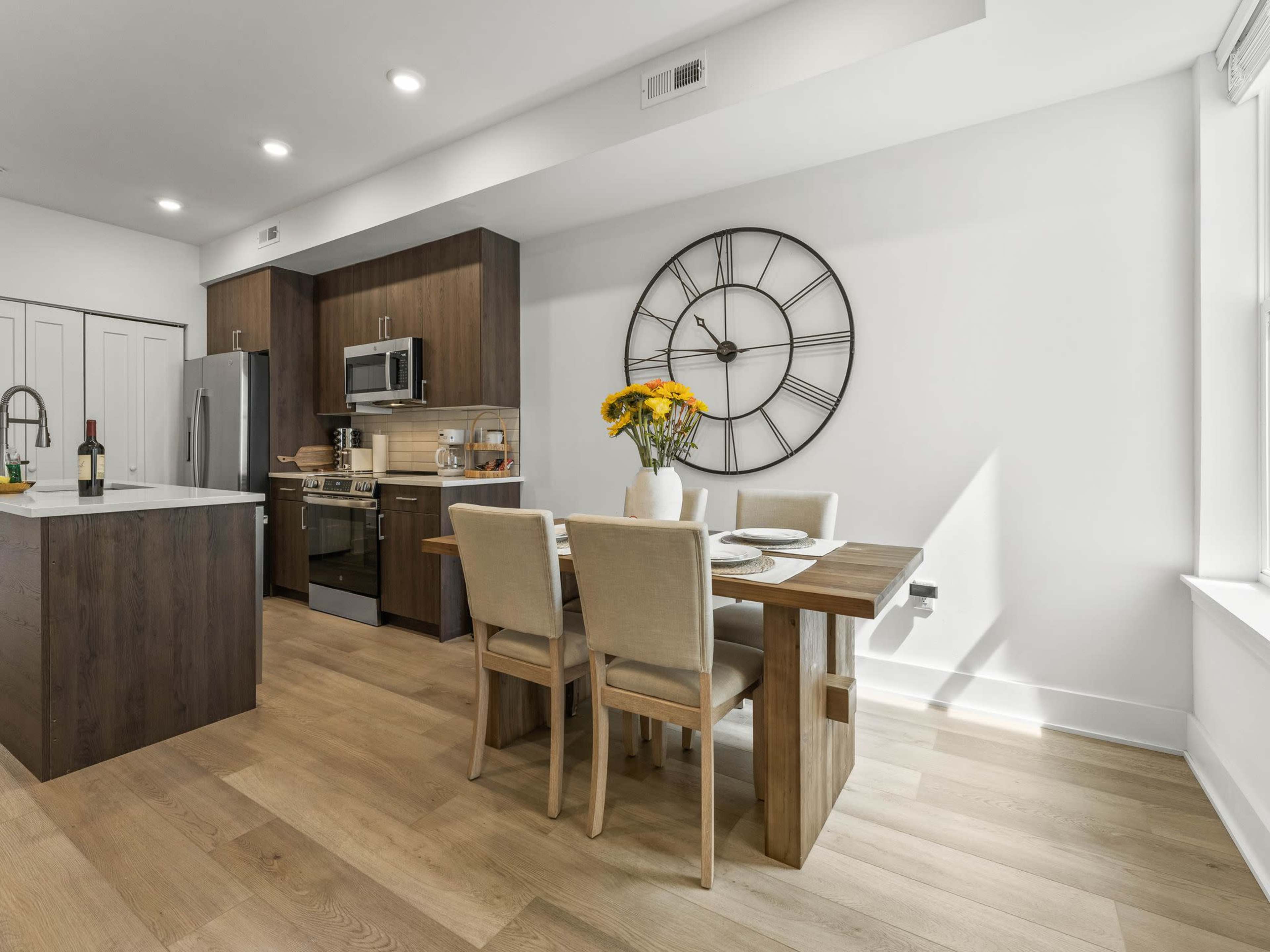 A modern kitchen features wooden cabinets, stainless steel appliances, and a dining table set for four with a floral centerpiece.