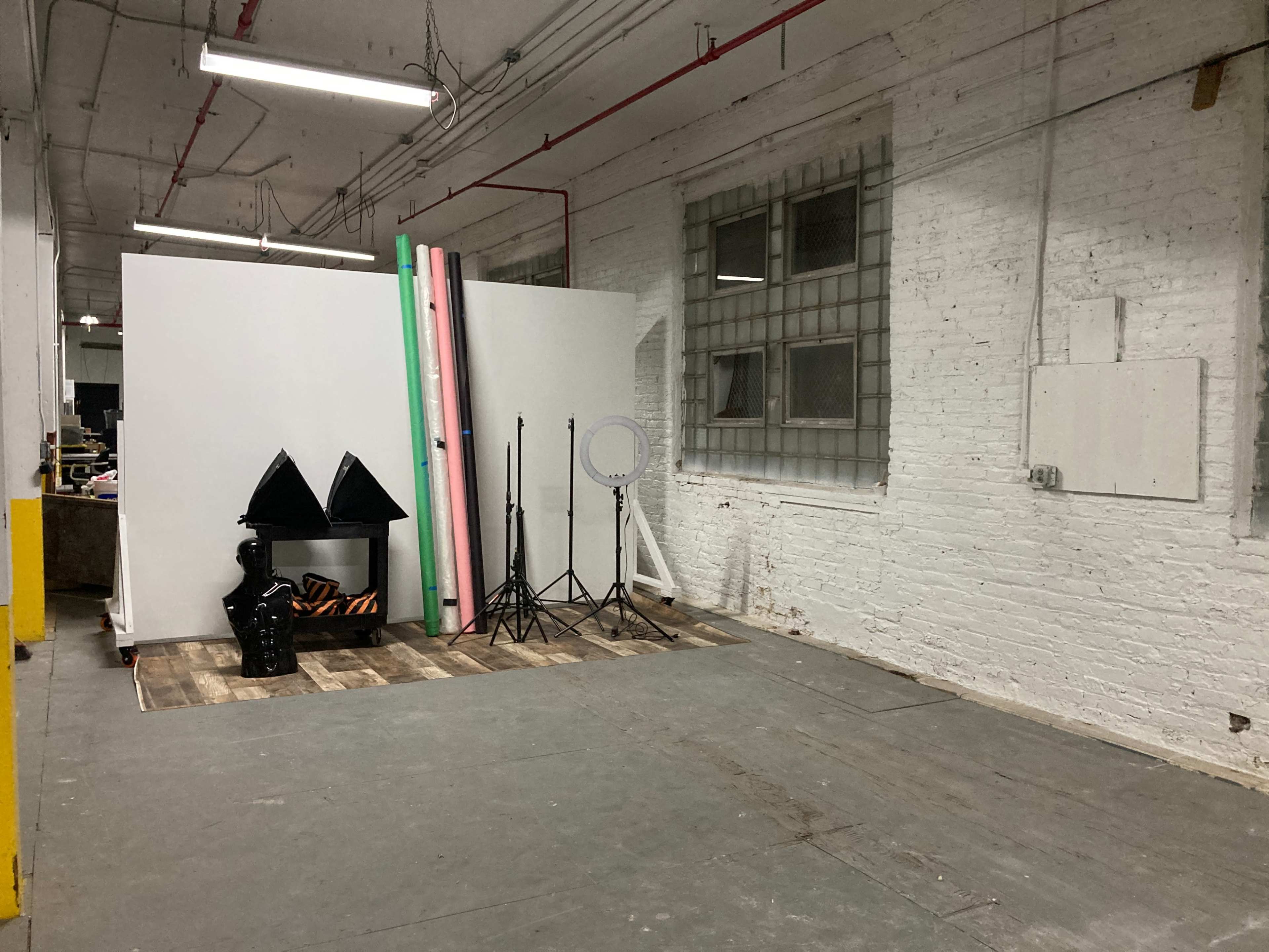 A studio space with blank backdrops, lighting equipment, and a wooden floor in a warehouse-like setting.