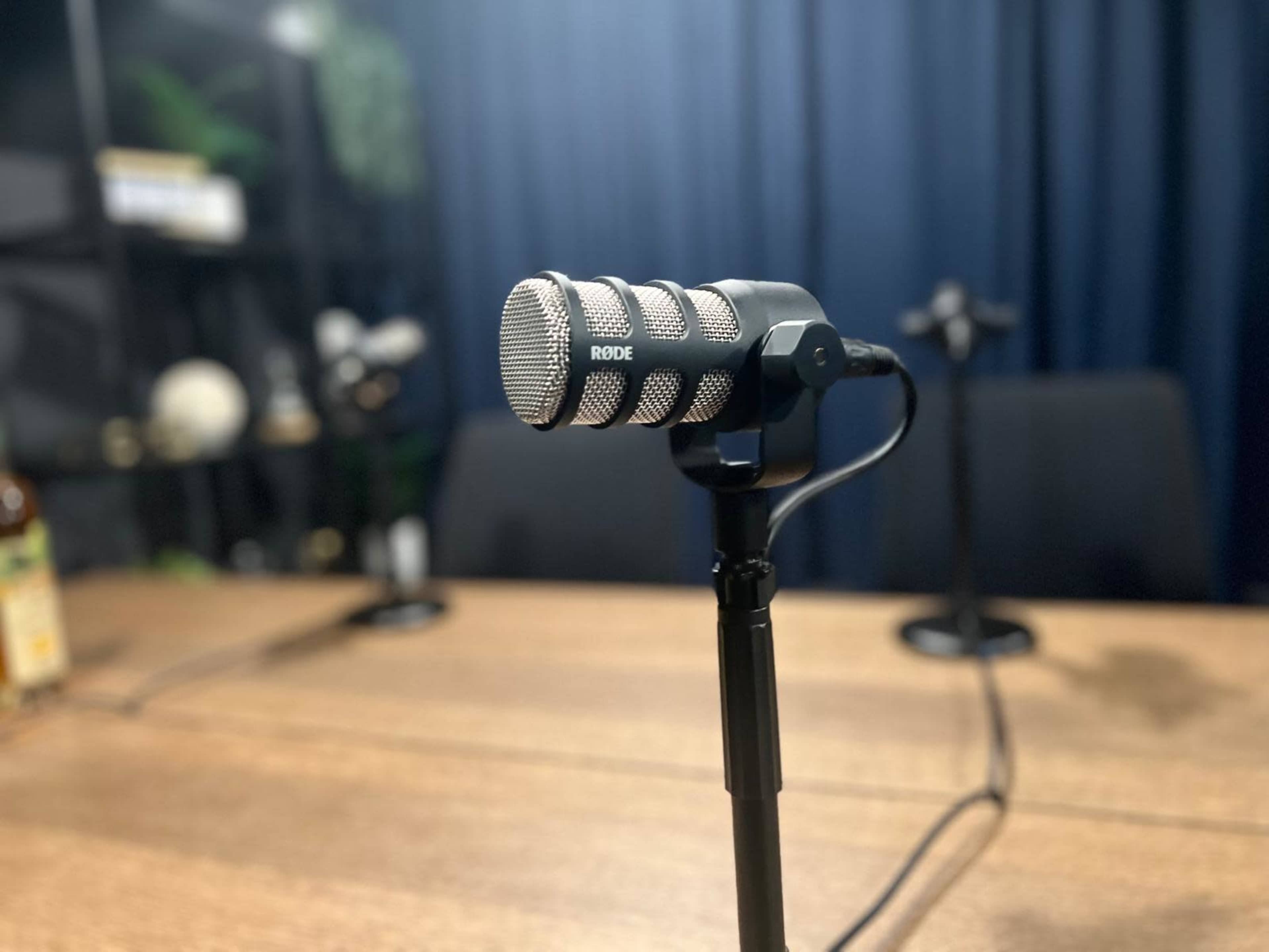 A Rode microphone is positioned on a table in a room with dark blue curtains in the background.