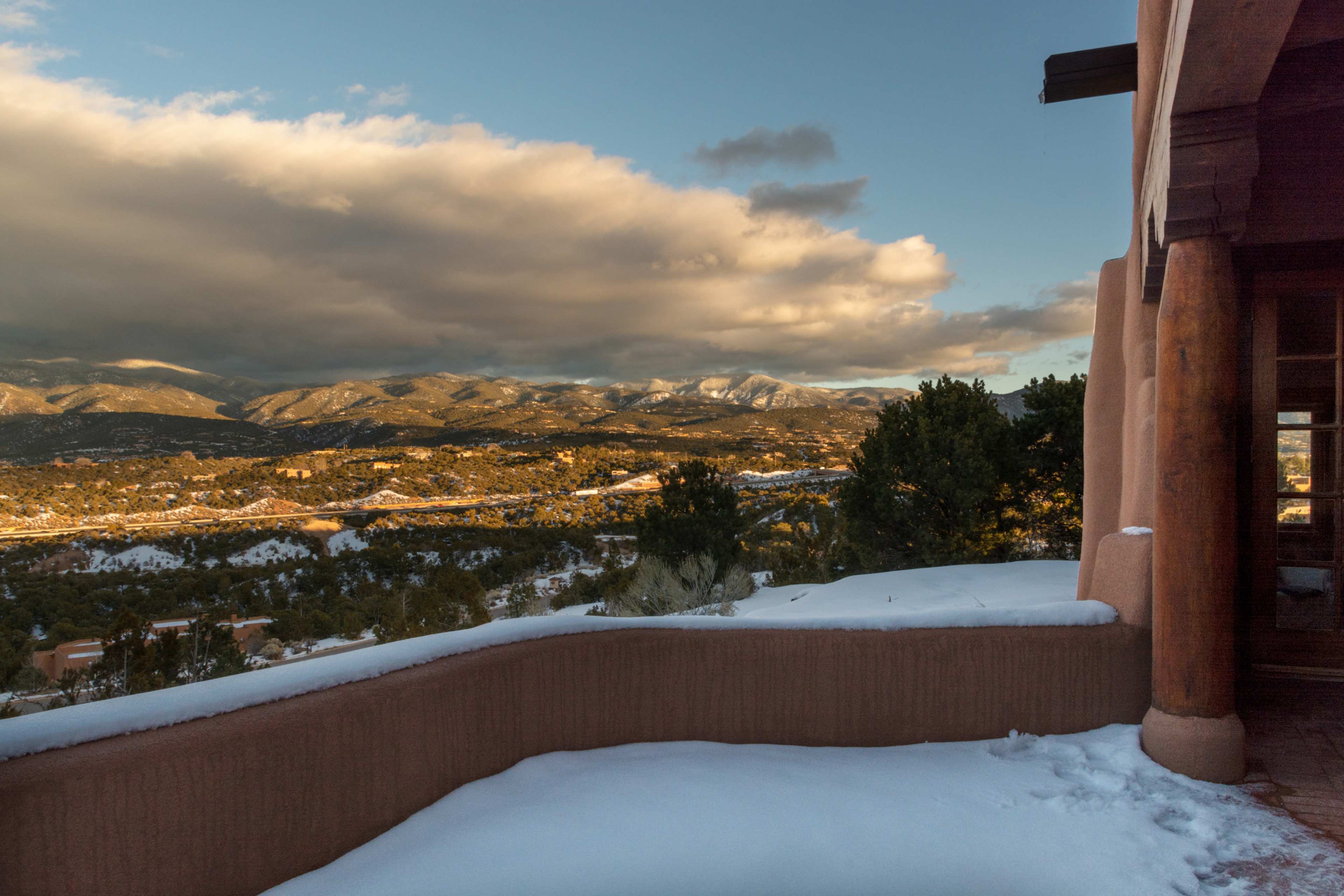A snow-covered balcony overlooking a mountainous landscape under a partly cloudy sky.